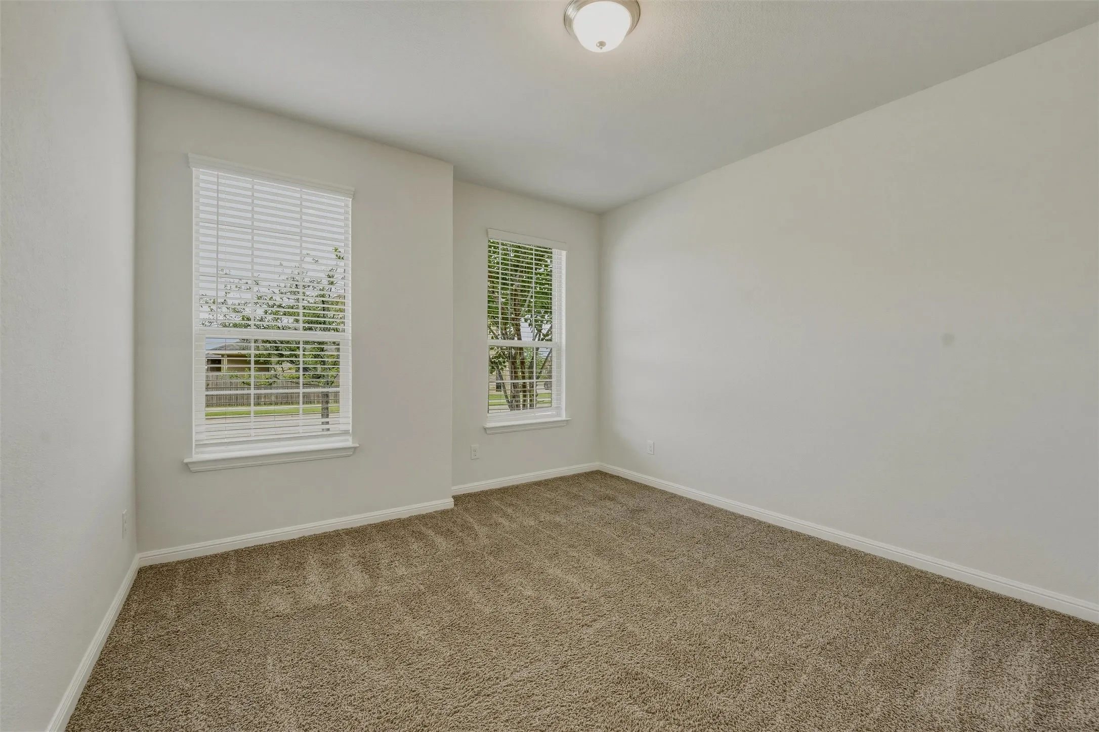 Carpeted room with white walls, two windows featuring horizontal blinds, and a flush-mount ceiling light fixture