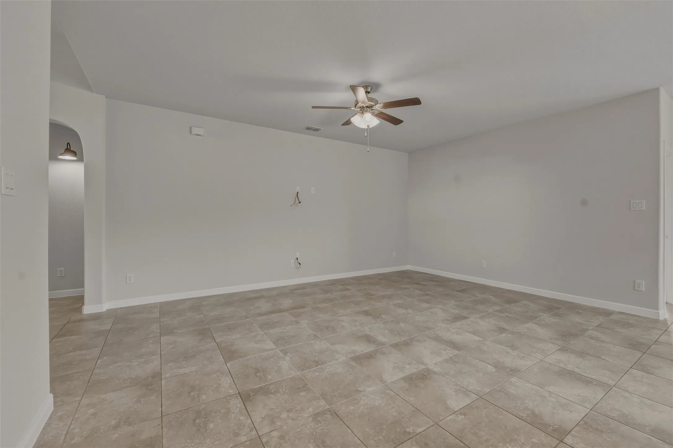 Spacious room featuring neutral-toned tile flooring, light gray wall paint, and a ceiling fan with integrated lighting