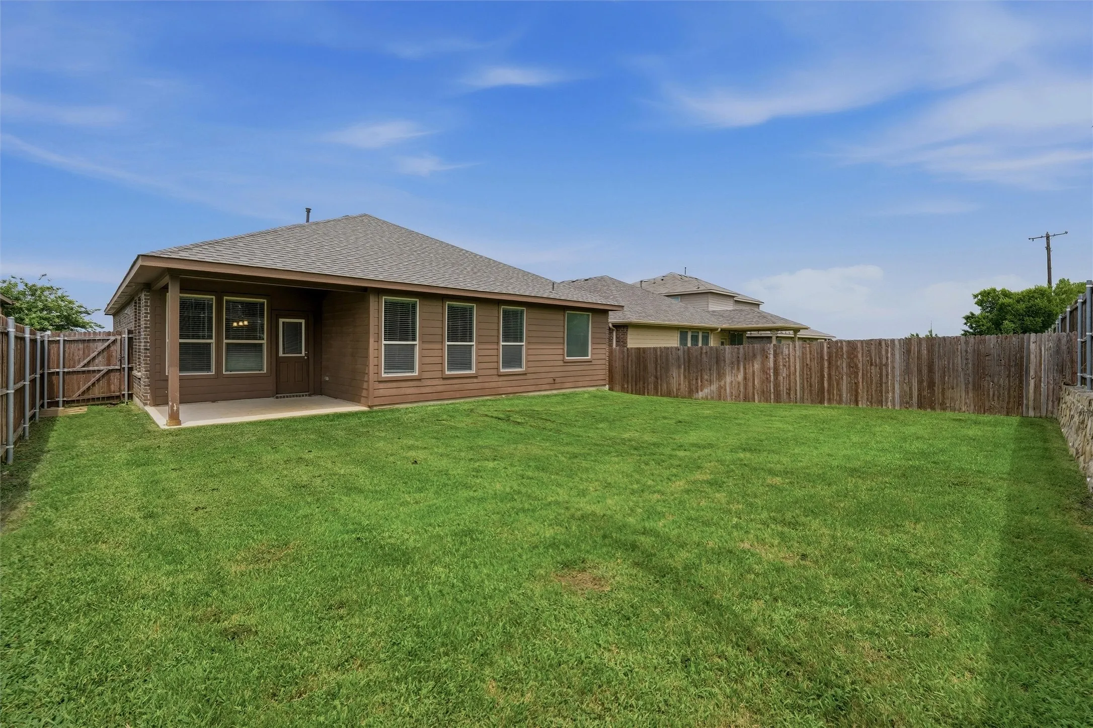Expansive backyard featuring a lush lawn, privacy fencing, and a covered concrete patio