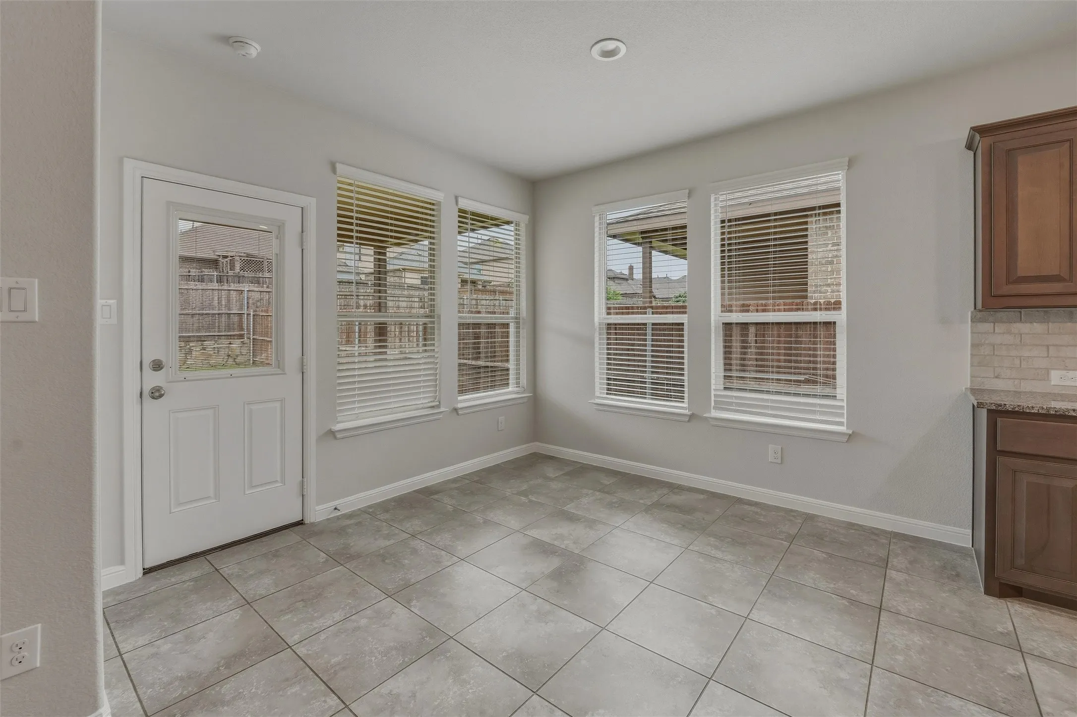 Room featuring light gray walls, gray square tile flooring, and multiple windows with blinds