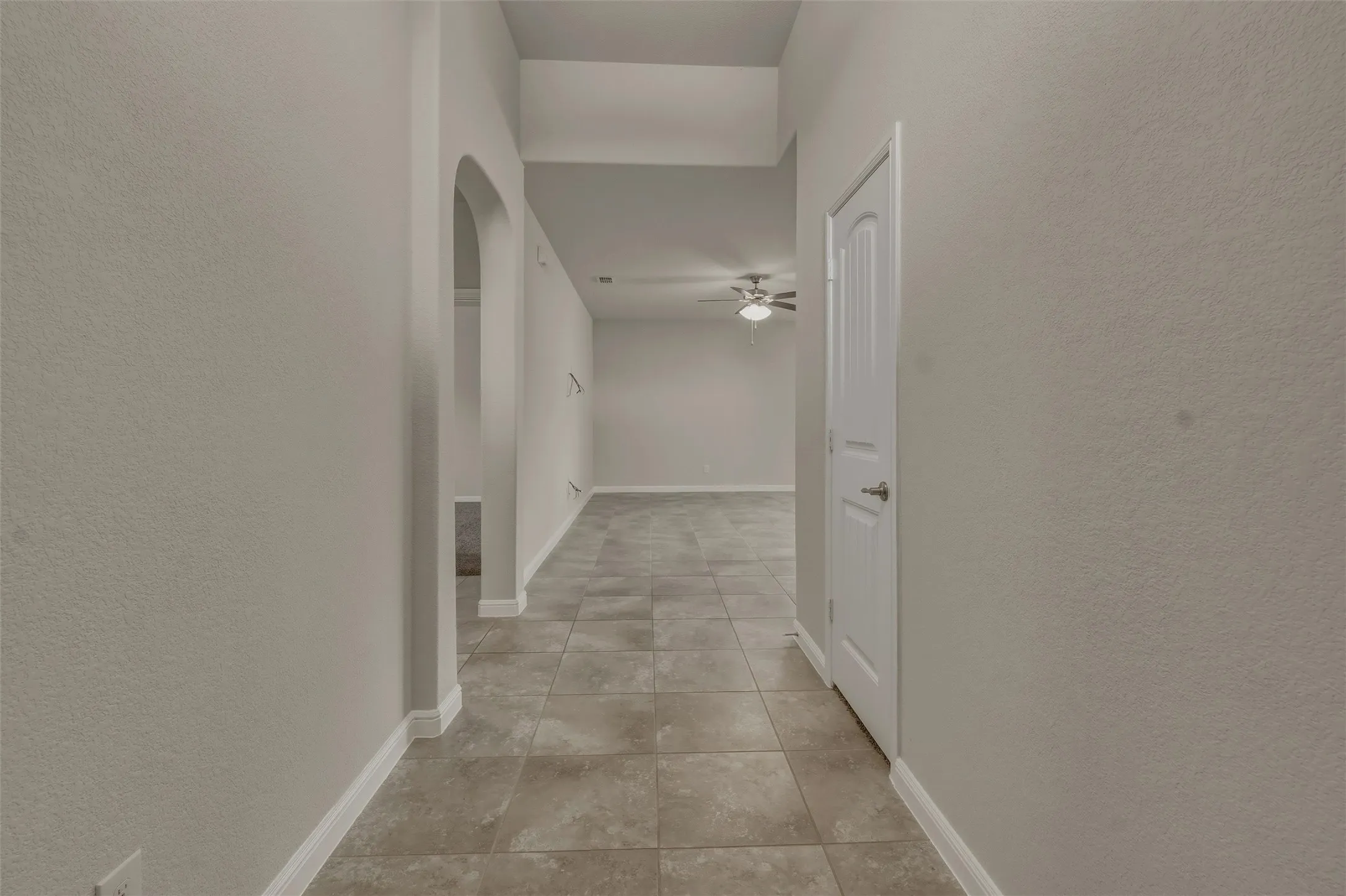 Tiled hallway featuring neutral wall tones, white baseboards, a white interior door, and an arched entryway