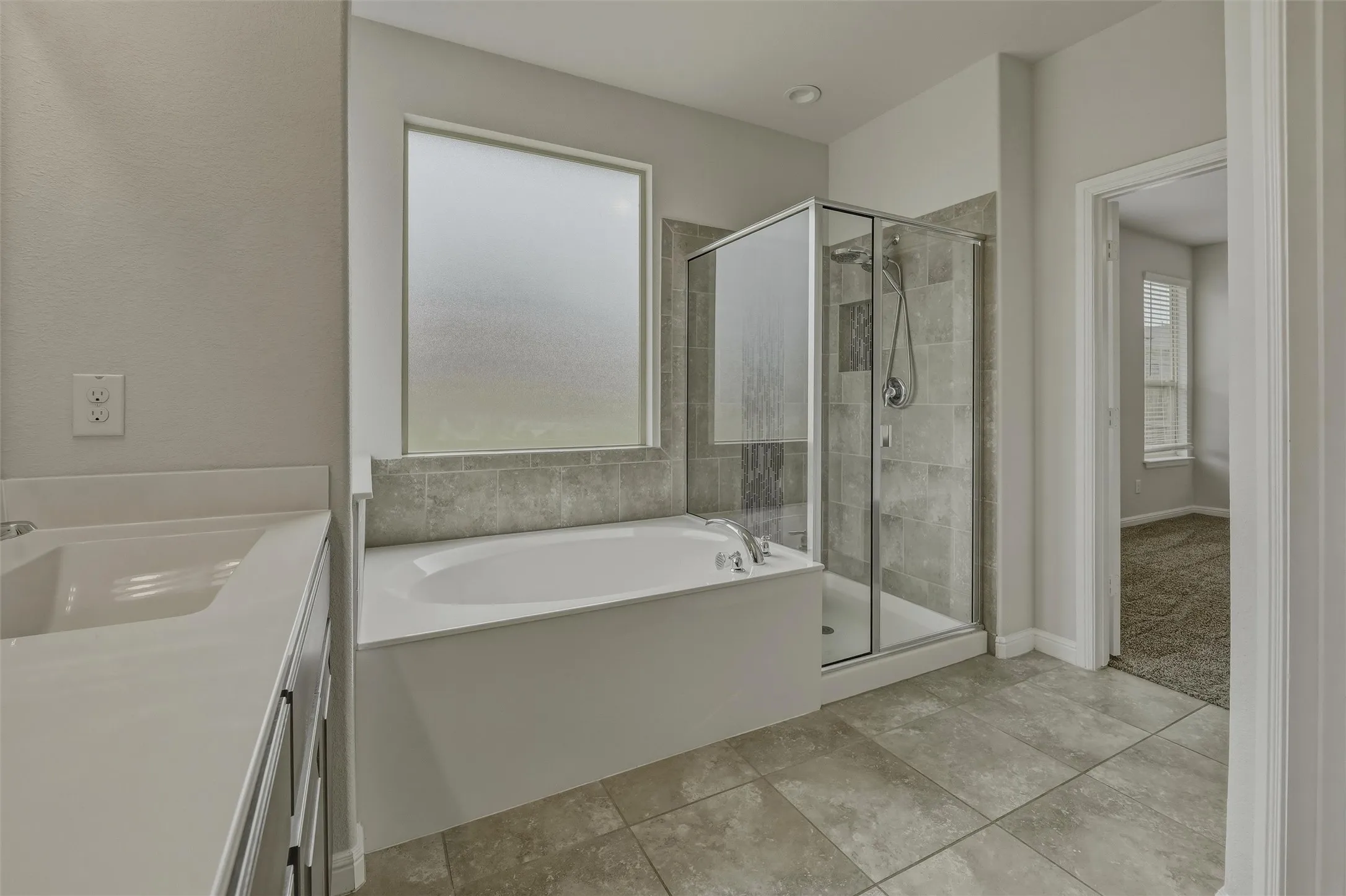 Bathroom featuring a built-in soaking tub with tiled surround, a glass-enclosed shower with tiled walls, and a vanity with a single basin
