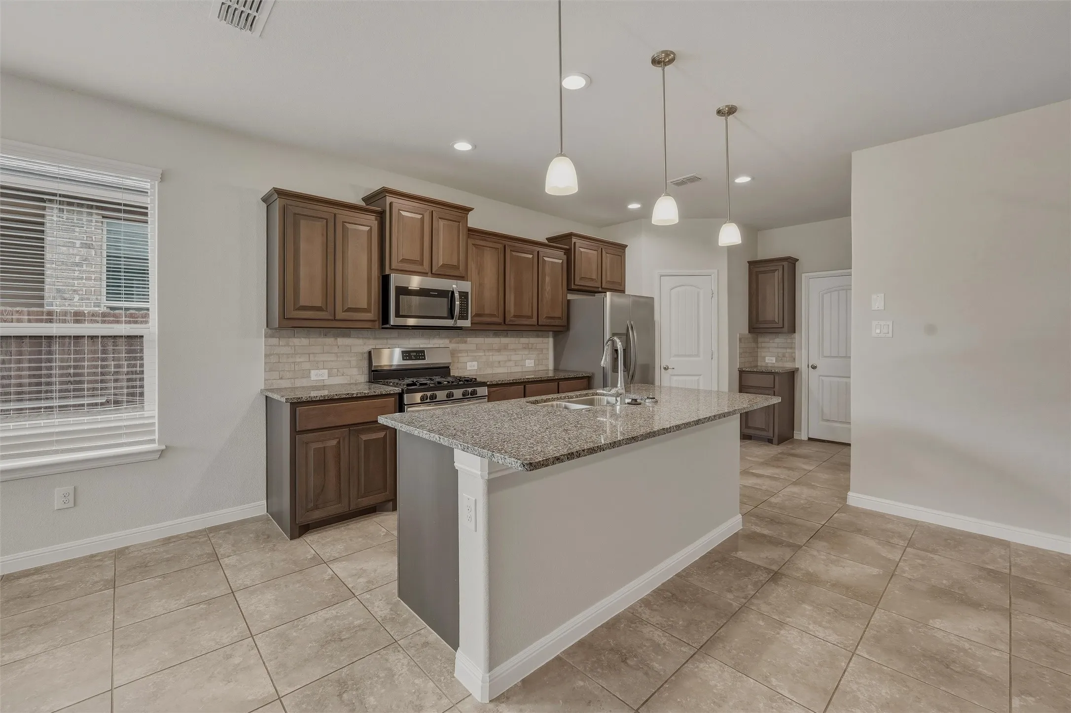 Kitchen featuring a central island with a sink, pendant lighting, stainless steel appliances, wood cabinetry, and a tile backsplash