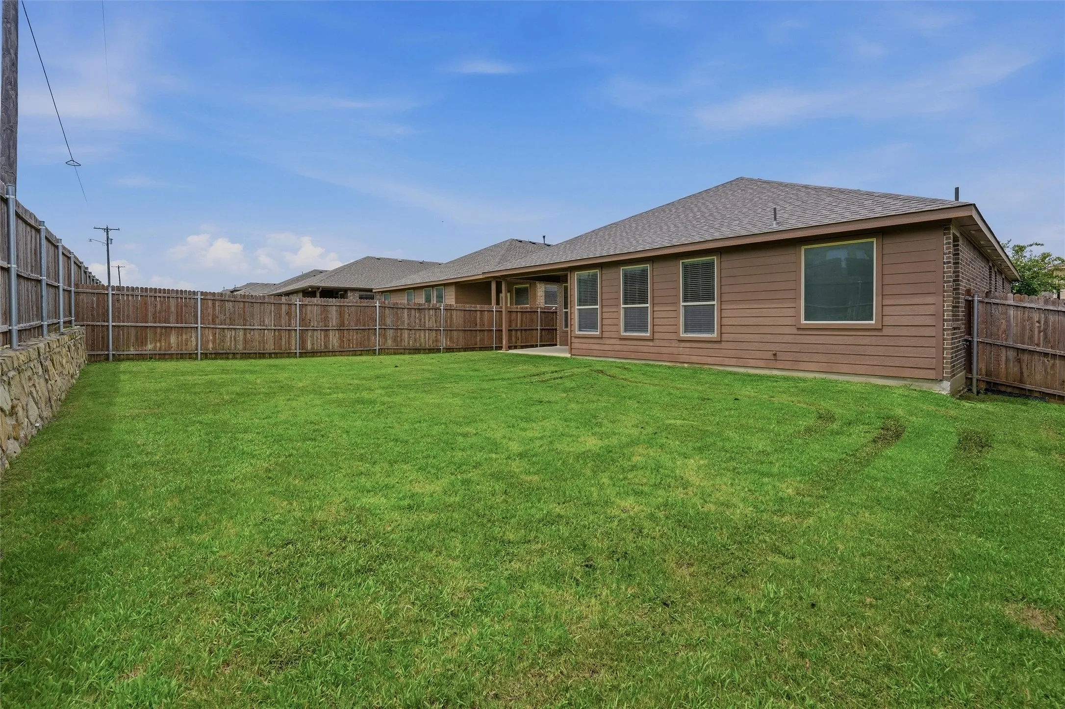 Expansive green lawn with a wood plank privacy fence and stone retaining wall