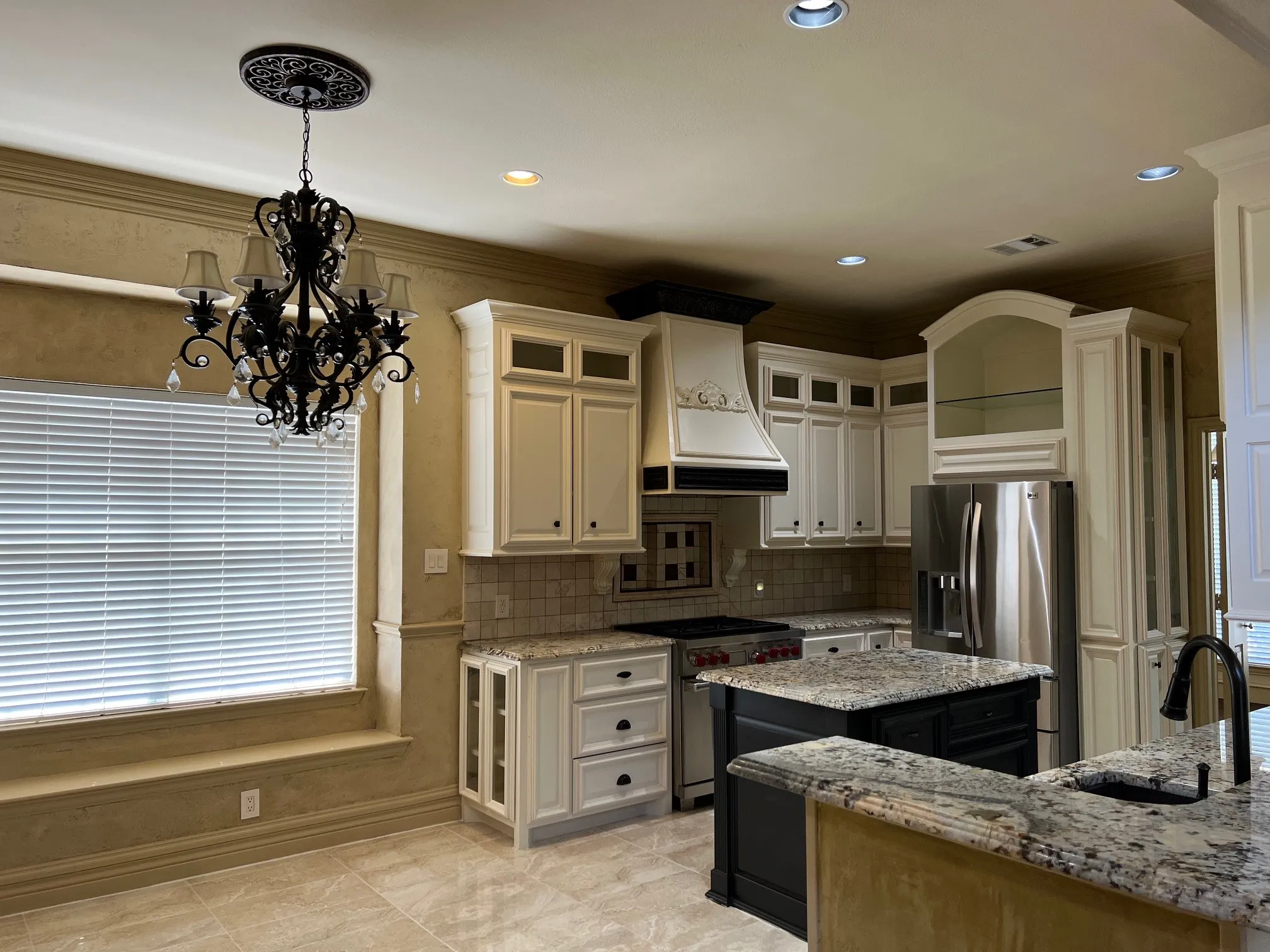 Kitchen featuring an inviting chandelier, light stone countertops, custom exhaust hood, stainless steel appliances, and sink