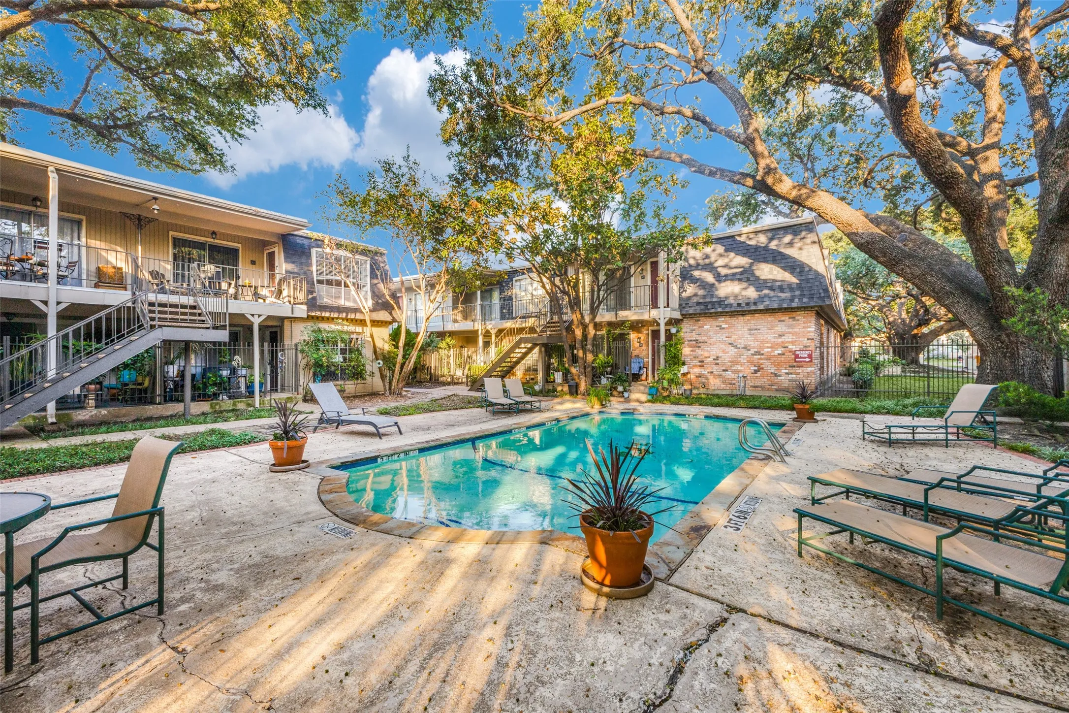 Central swimming pool surrounded by concrete decking and mature trees