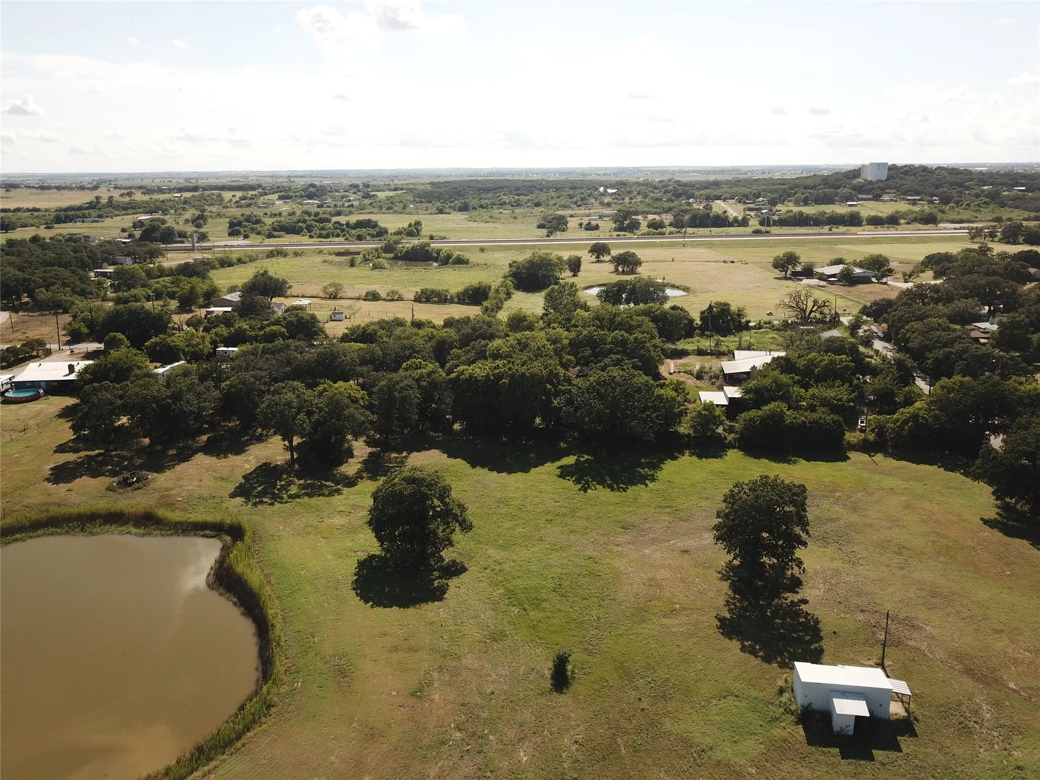 Expansive land featuring a prominent pond, mature trees, open grassy areas, and a visible utility structure