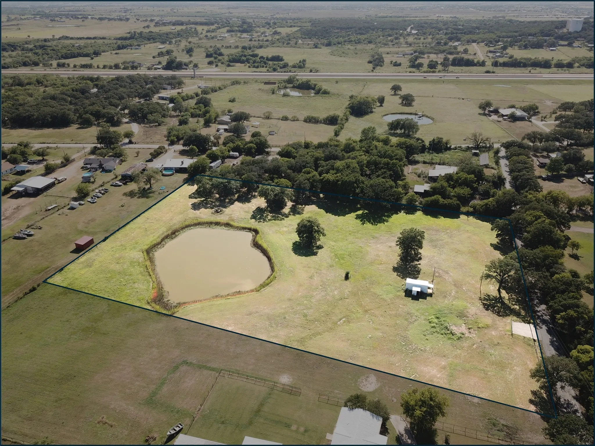 Eastern view of acreage featuring a large pond, mature trees, and a distant tollroad - perimeter is an estimate