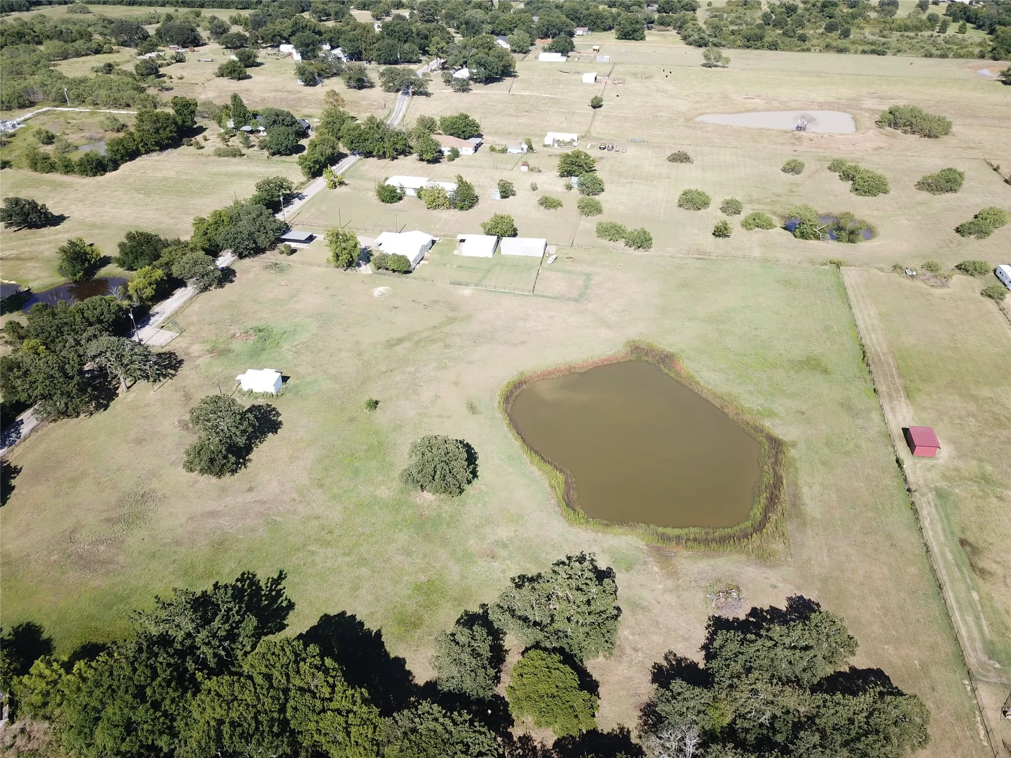 Expansive acreage featuring a natural pond, scattered mature trees, and multiple outbuildings