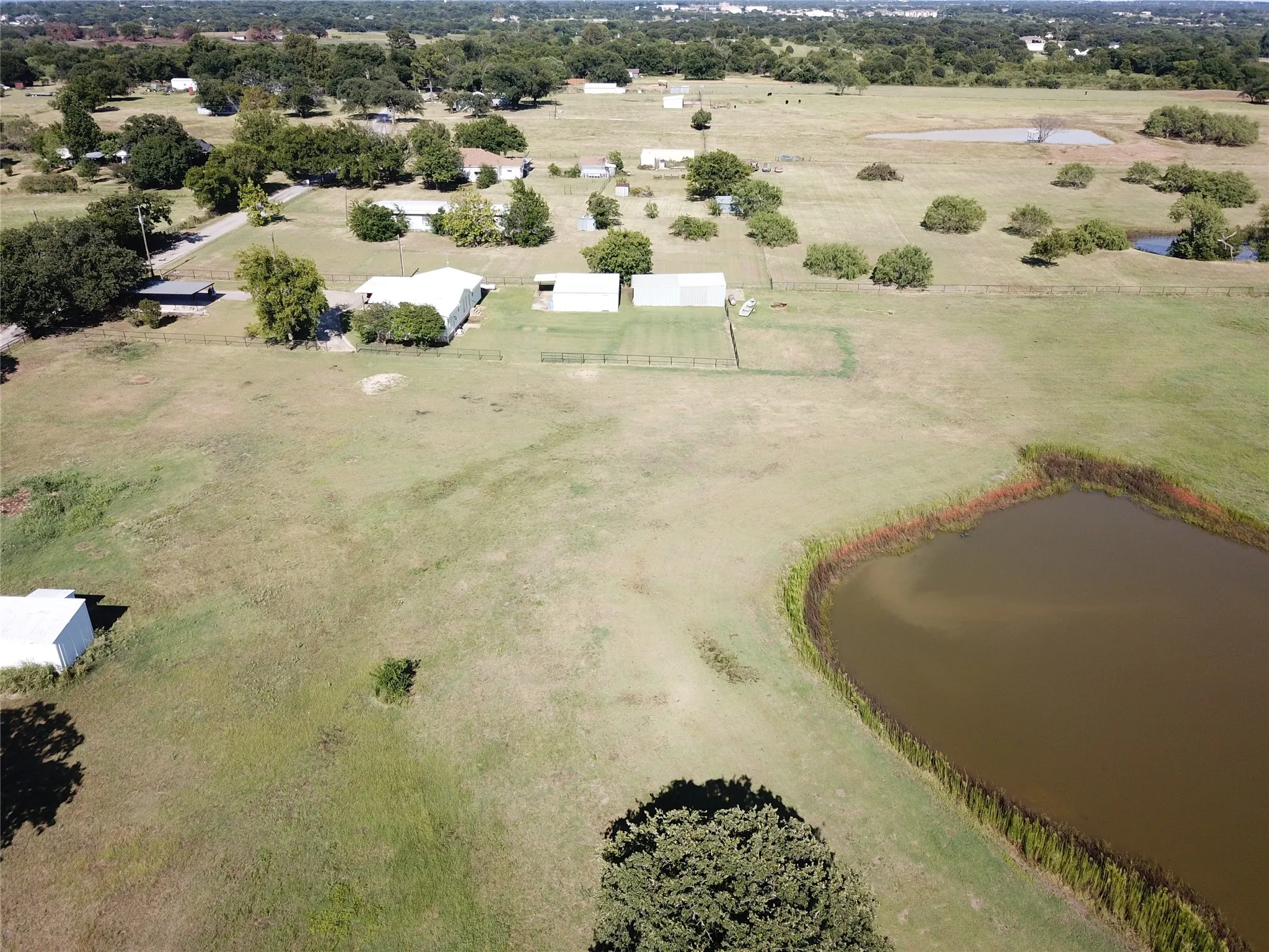 Expansive property featuring a private pond with natural reeds, open fields, mature trees, and neighboring properties