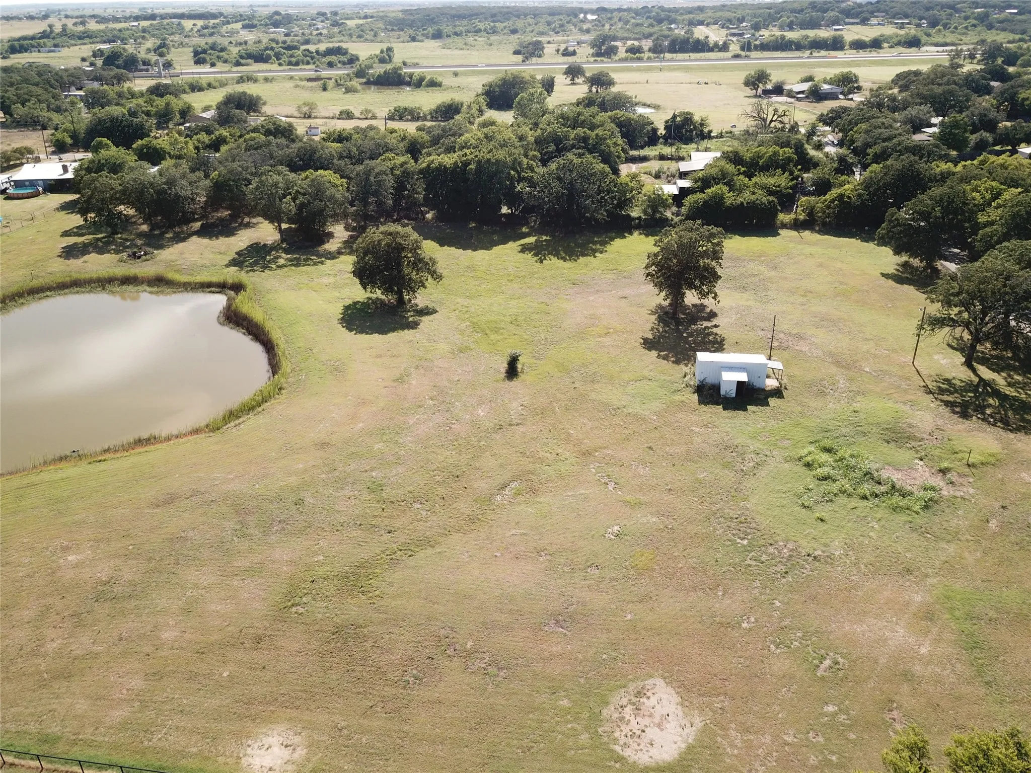 Expansive property featuring a deep pond, mature trees, and a utility structure