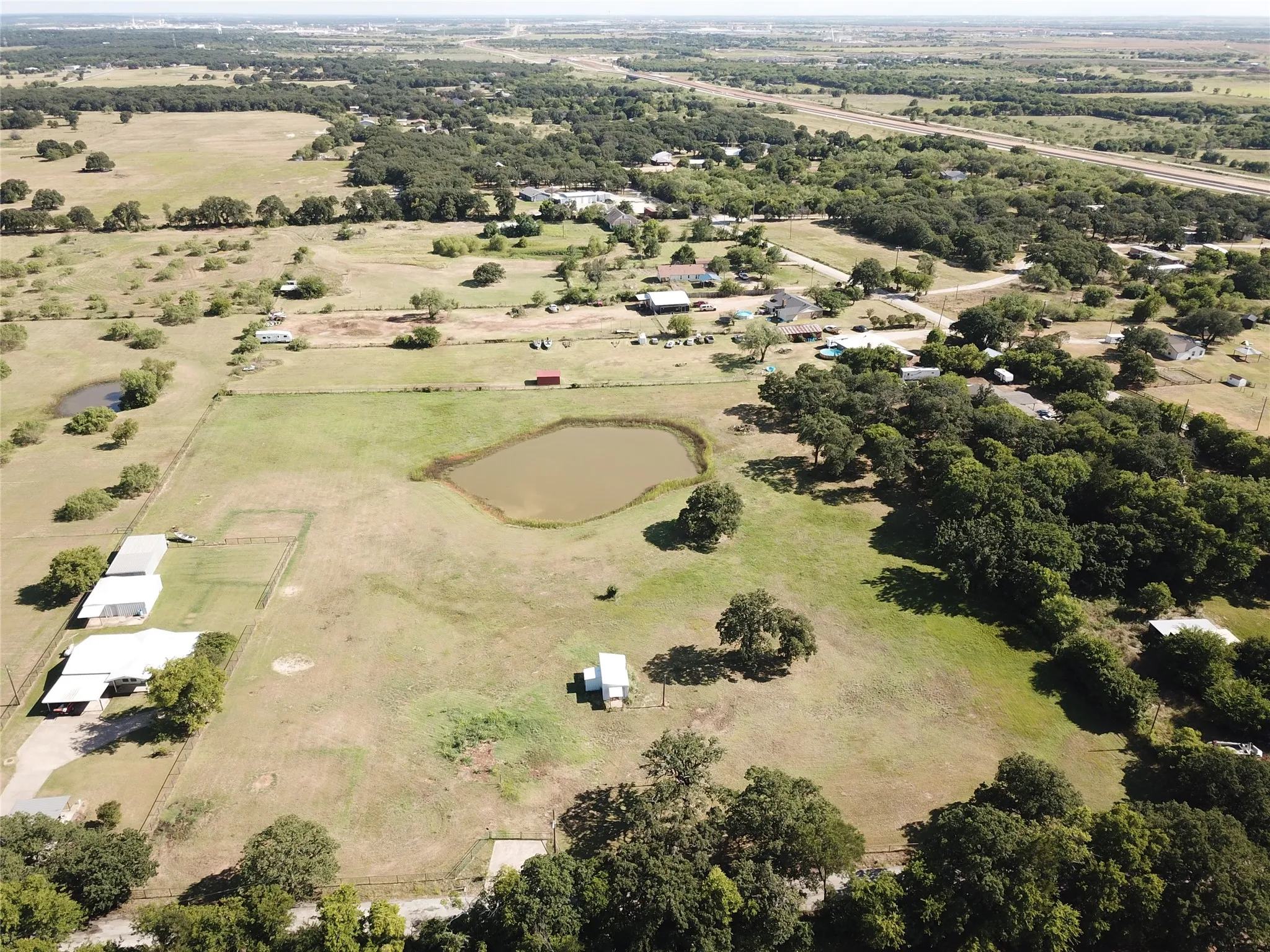 Expansive aerial view of a rural property featuring multiple outbuildings, mature trees, and a private pond