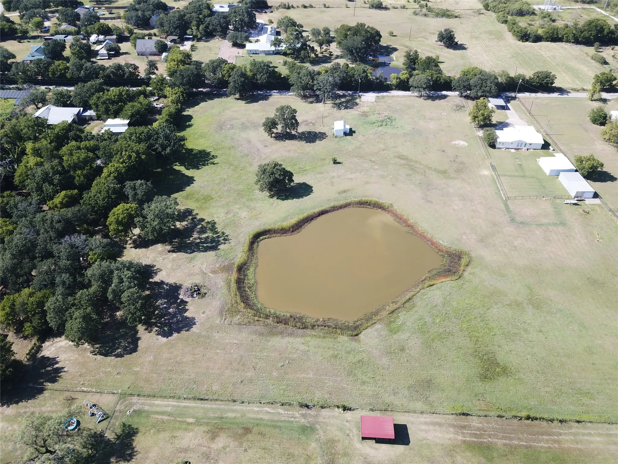Back view of property featuring a large pond, surrounding green space, and mature trees