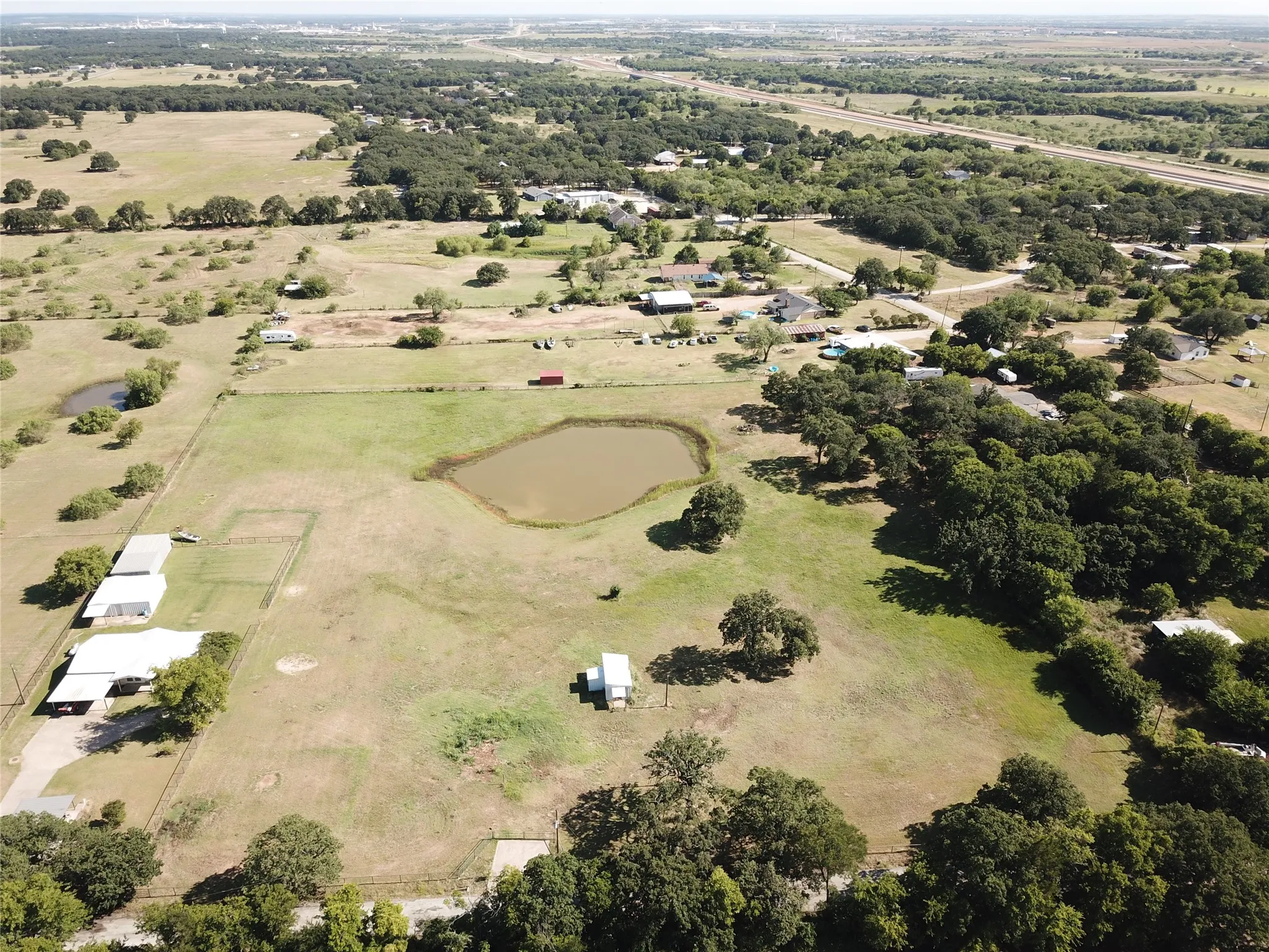 Front view of acreage featuring a large pond, mature trees, and storage building