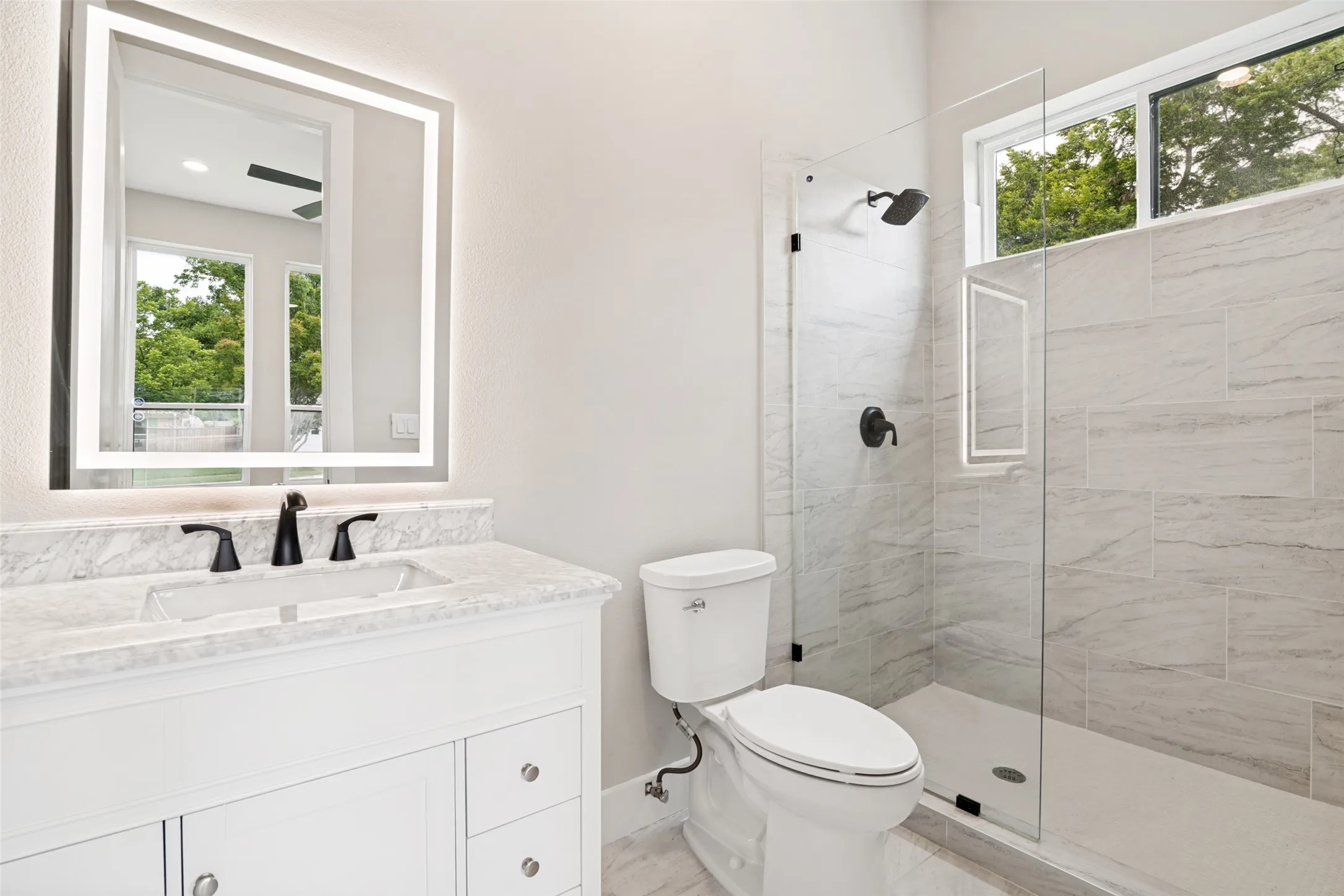 Bathroom featuring a white vanity with a light-toned countertop, a backlit mirror, and a glass-enclosed shower