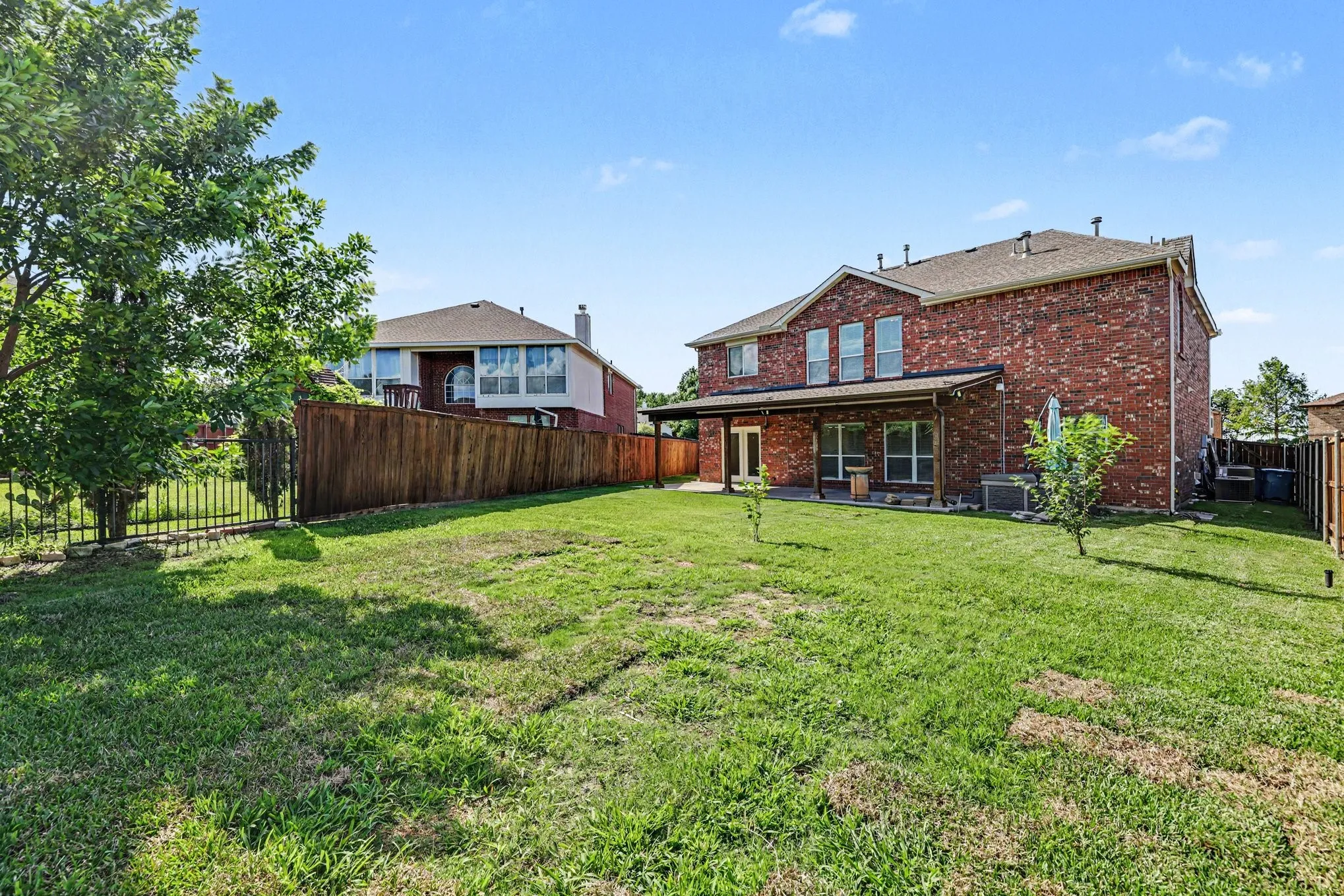 Expansive backyard featuring a manicured lawn, brick exterior, covered patio, and privacy fencing