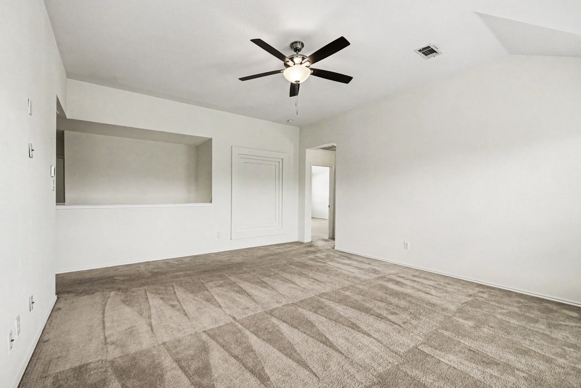 Spacious room featuring patterned carpet flooring, a ceiling fan with integrated lighting, and a recessed wall niche
