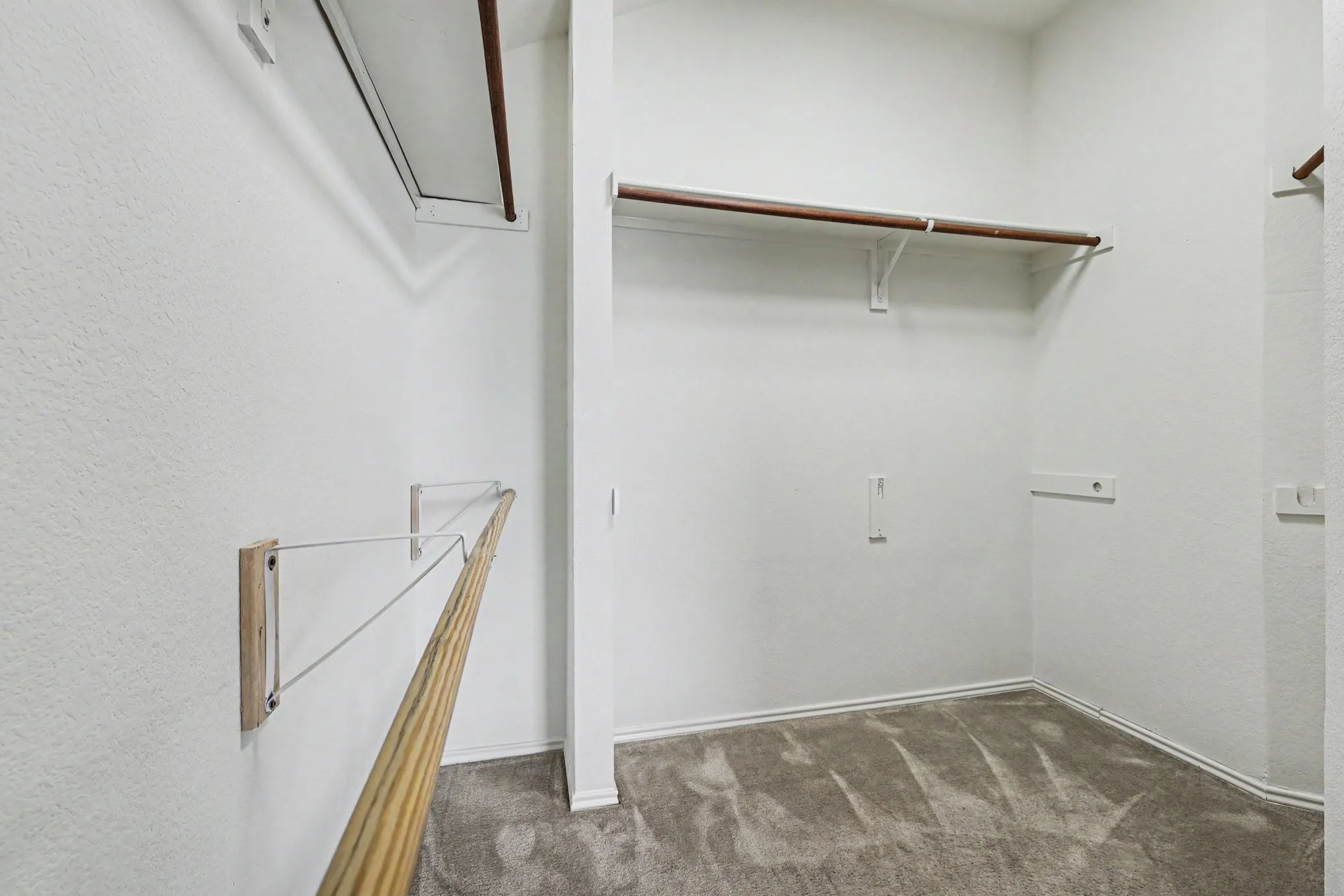 Walk-in closet featuring light gray carpeting, multiple clothing rods, and white walls