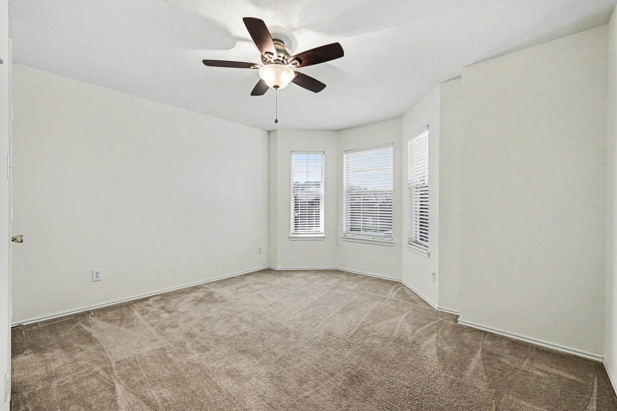 Carpeted room featuring a ceiling fan with integrated lighting, a bay window with three distinct window units, and white horizontal blinds