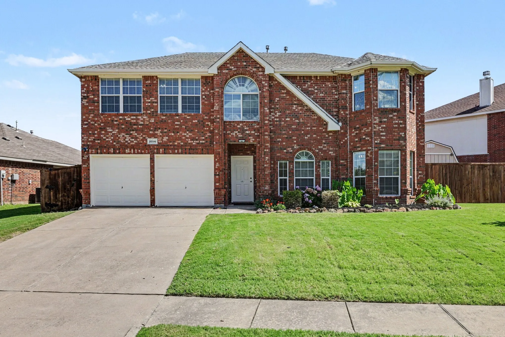 Brick facade residence featuring a two-car garage, concrete driveway, and front lawn