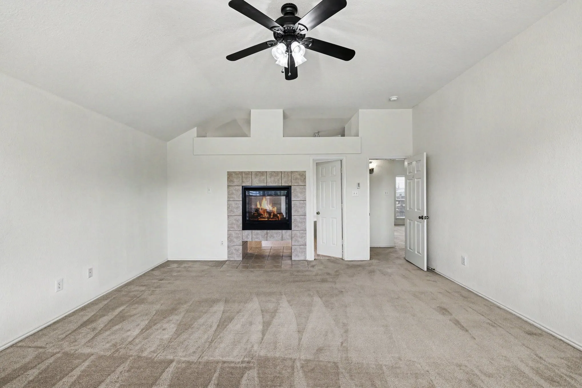 Spacious room featuring vaulted ceilings, a central ceiling fan with integrated lighting, and neutral carpeting