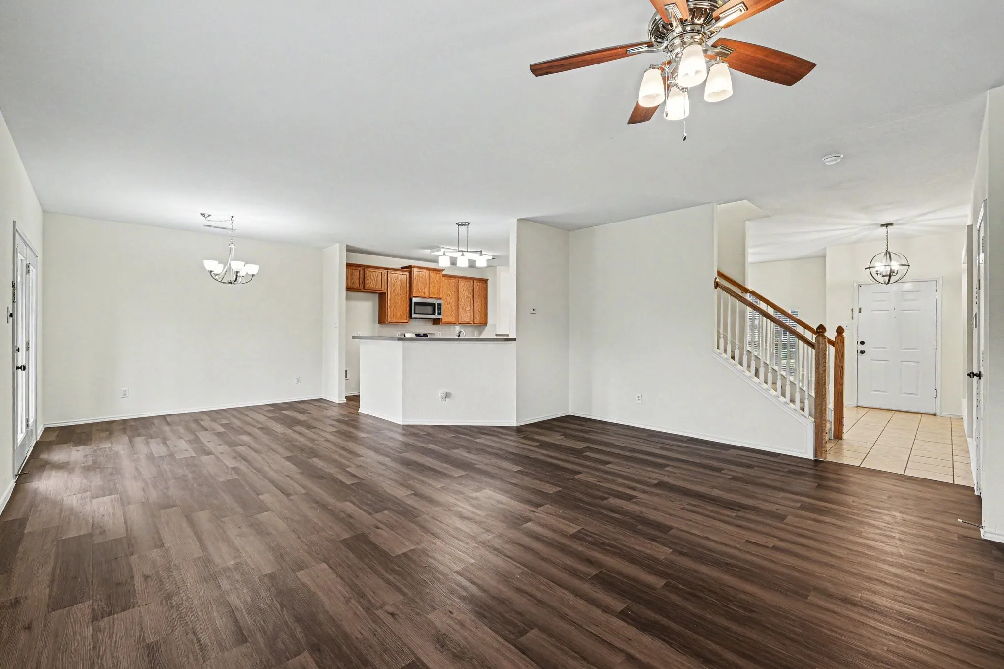 Spacious living area featuring wood-finish flooring, ample wall space, and a ceiling fan with integrated lighting
