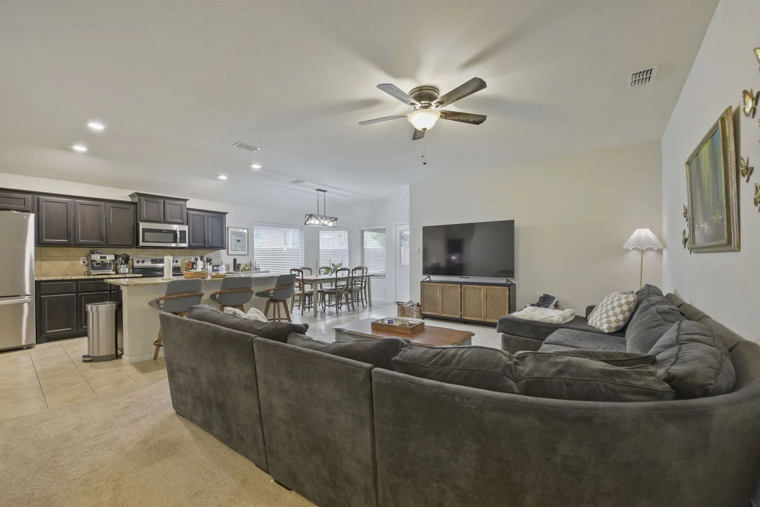 Open-concept living area with vaulted ceilings, featuring a kitchen island with seating, dark wood cabinetry, stainless steel appliances, and tile flooring