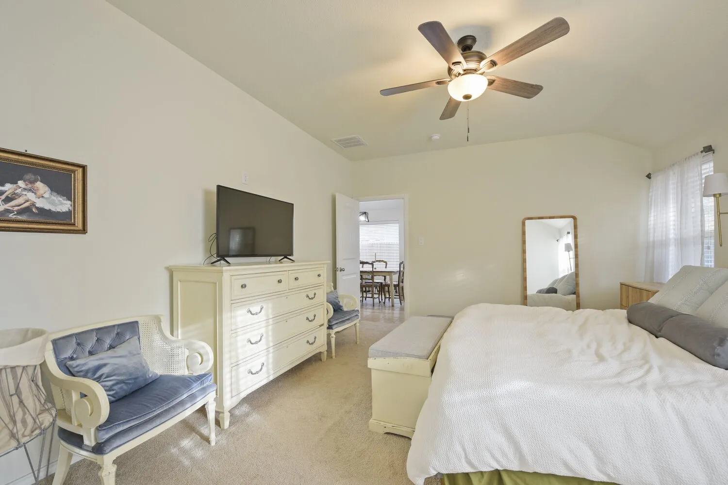 Vaulted ceiling bedroom featuring a ceiling fan with integrated lighting, soft carpet flooring, a wall-mounted television, and an open doorway to an adjacent space