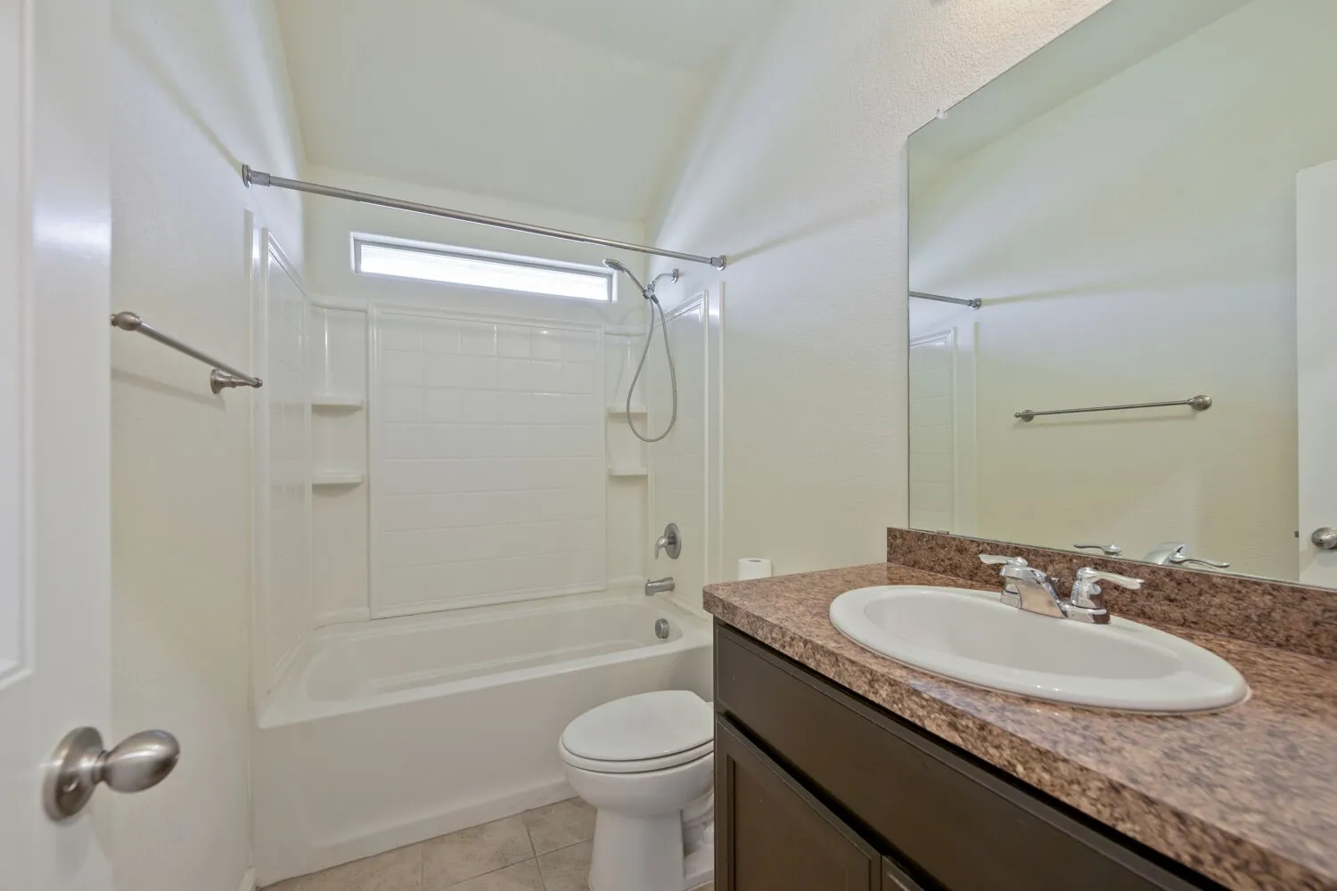 Bathroom featuring a white tub and shower combination with an overhead window, a vanity with a granite-style countertop, an integrated sink, and a large mirror