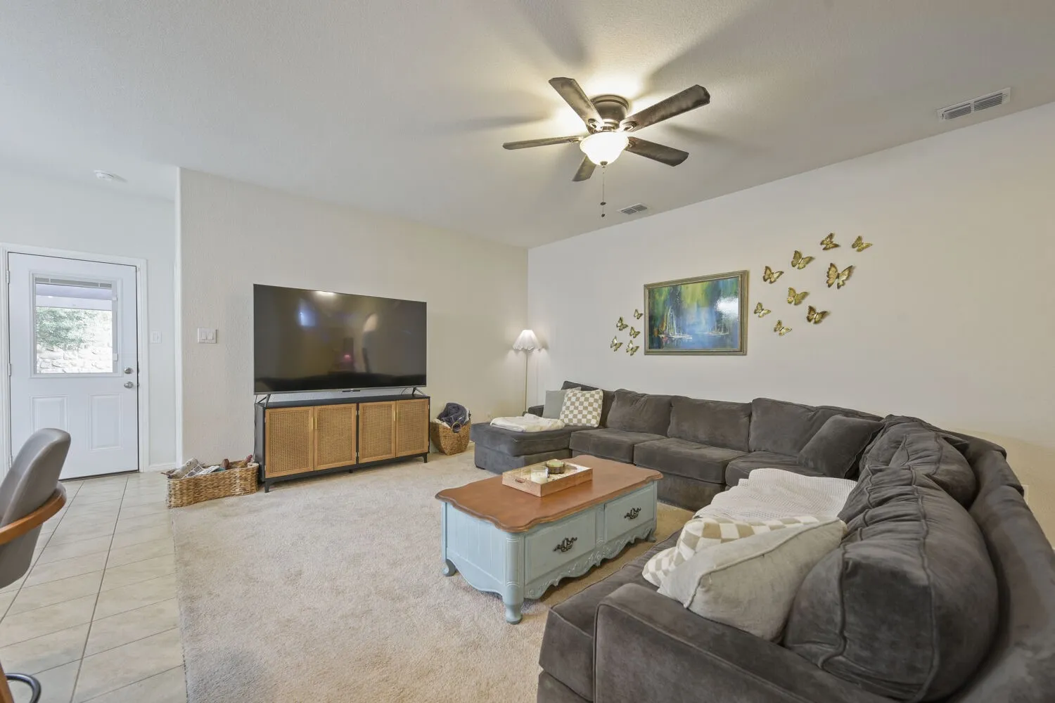 Spacious living area featuring a ceiling fan, carpet flooring, and a white paneled door with glass insert