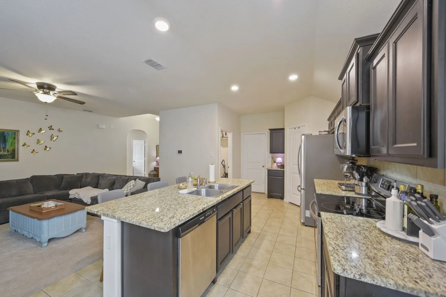 Open-concept kitchen and living area featuring granite countertops, dark wood-finish cabinetry, stainless steel appliances, and recessed lighting