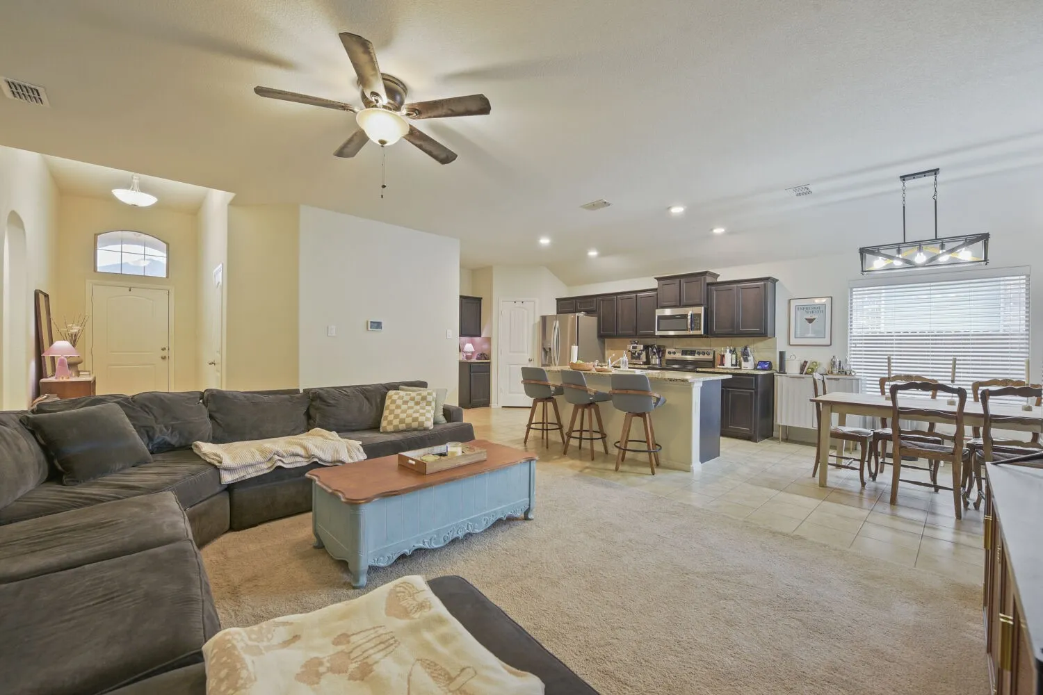 Open-concept living space featuring a living area with carpet, a ceiling fan, and an arched entry
