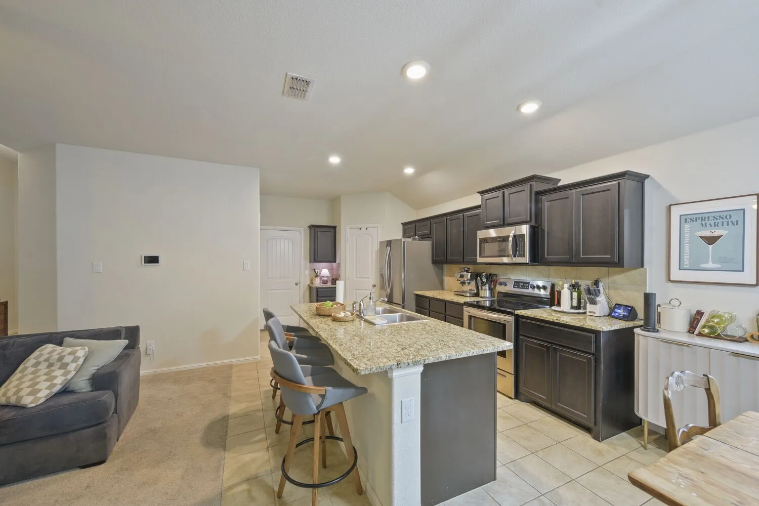 Open-concept kitchen featuring an eat-at island with granite countertop, dark wood cabinetry, stainless steel appliances, and recessed lighting