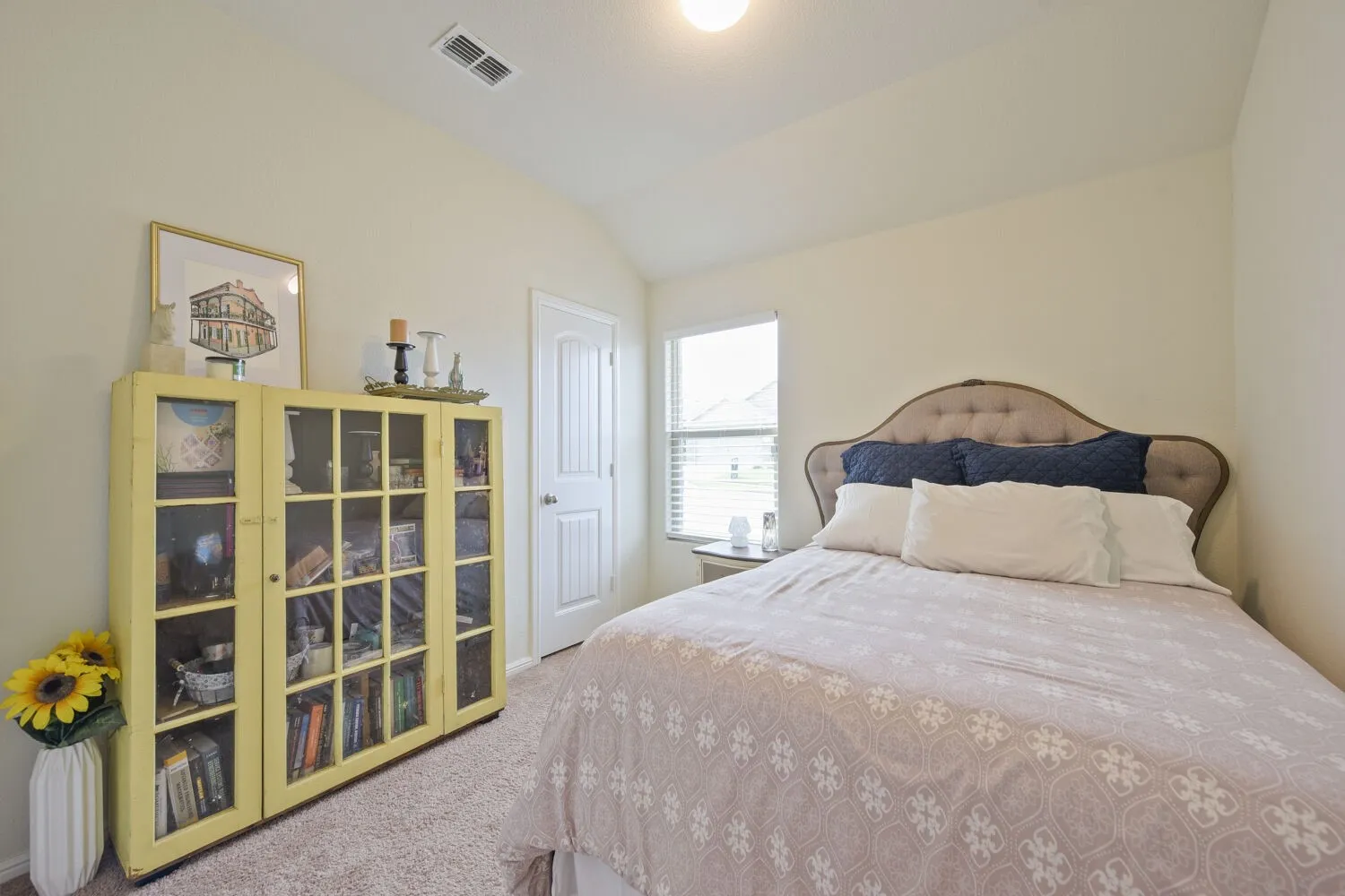 Carpeted bedroom featuring a vaulted ceiling, a single window with blinds, and a white interior door