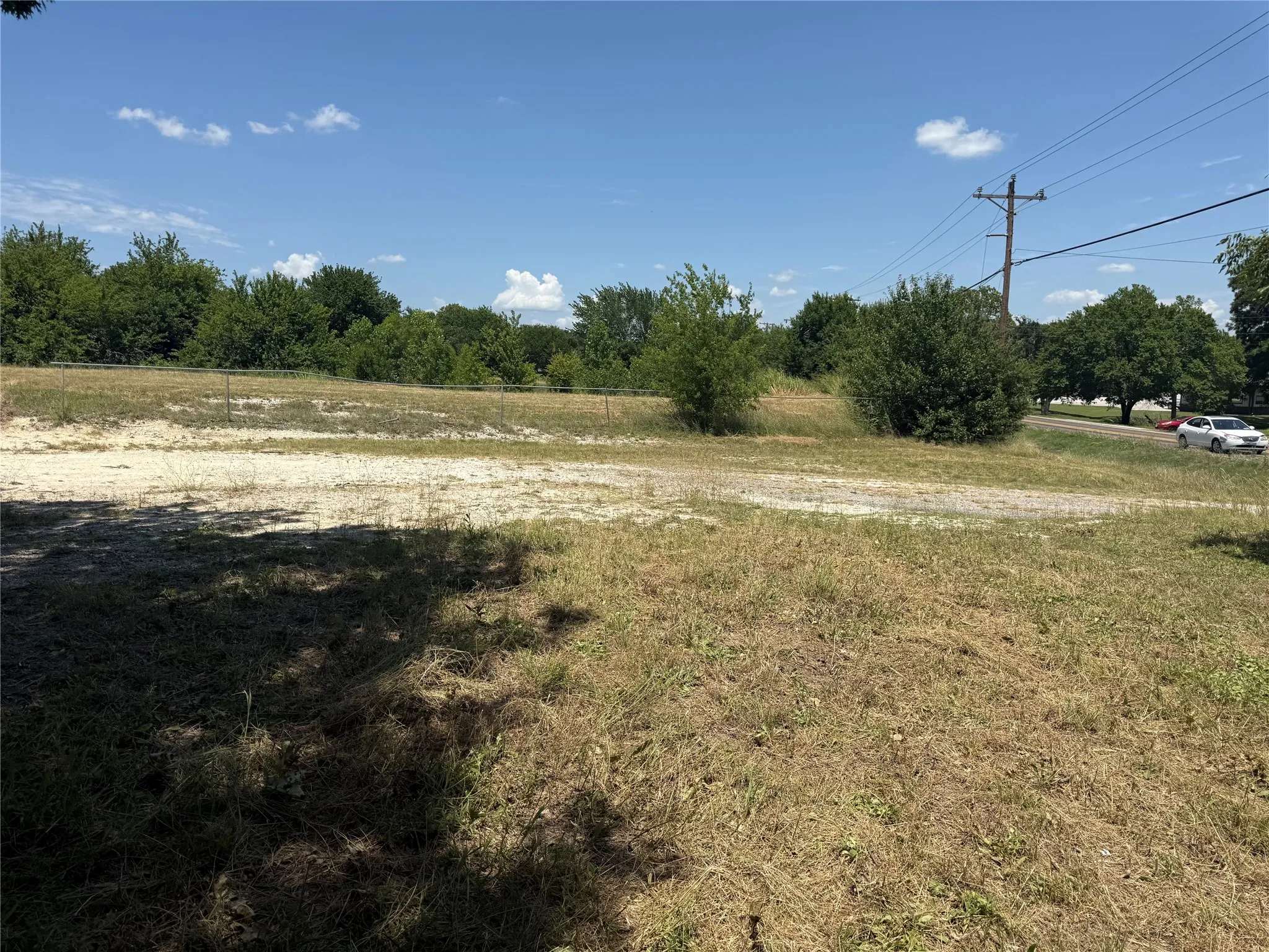 Expansive land parcel featuring natural ground cover, mature trees along the perimeter, and a clear blue sky overhead