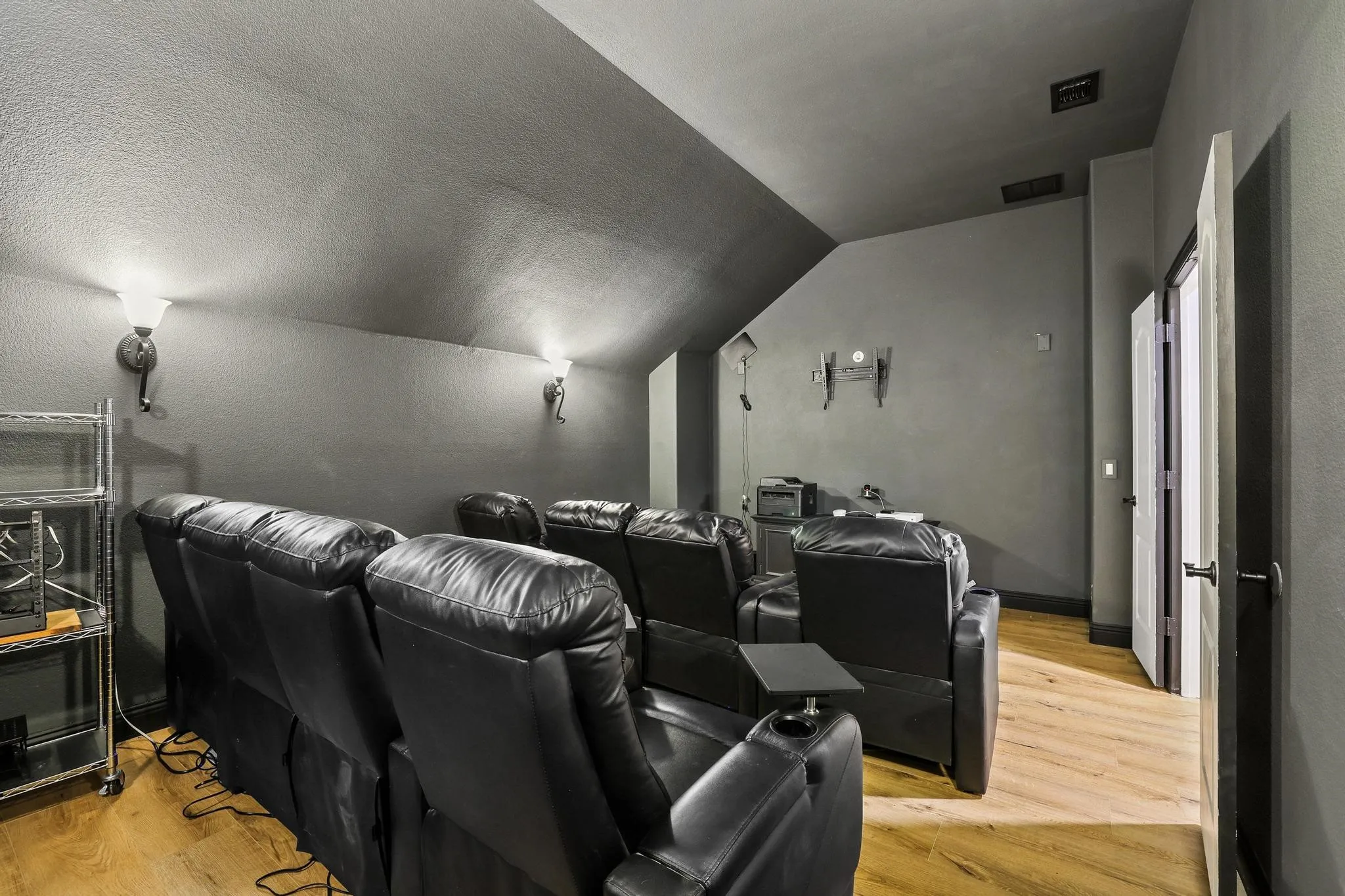 Dedicated media room featuring wood-finish flooring, dark gray walls, and sconce lighting