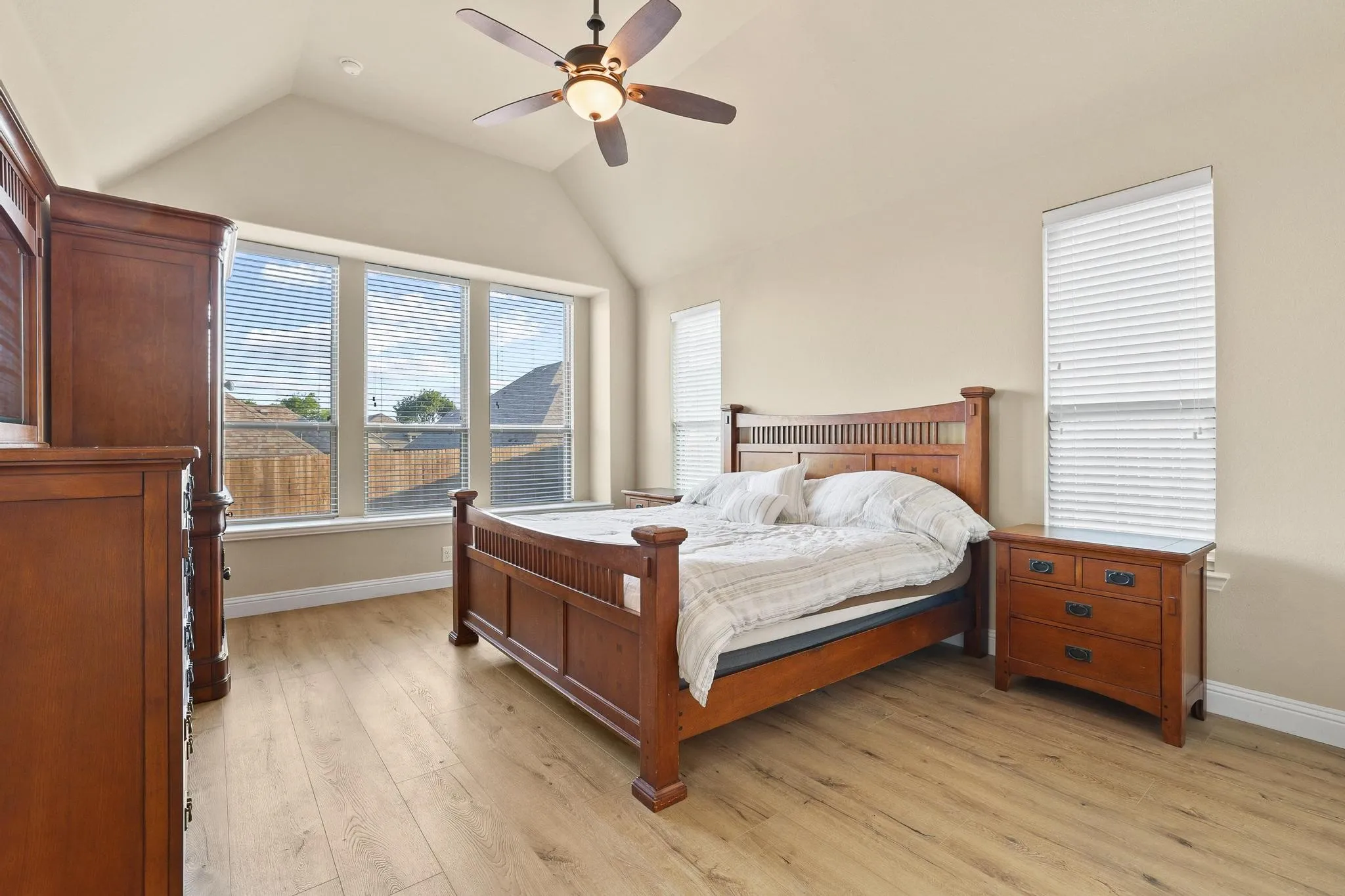 Vaulted ceiling with a ceiling fan, light wood-finish flooring, and multiple windows with blinds