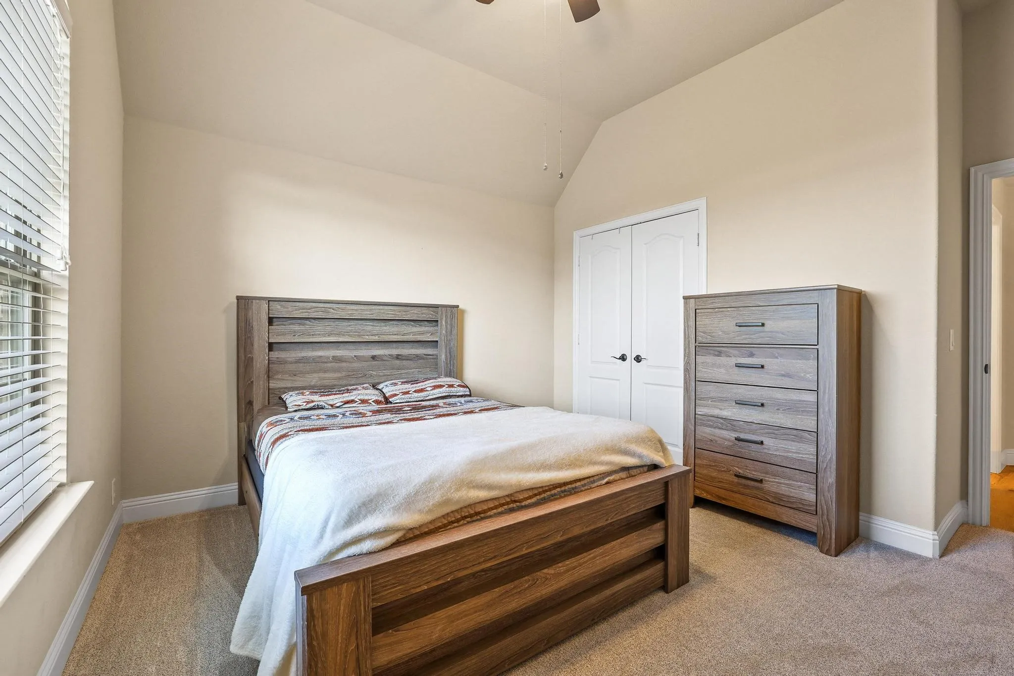 Carpeted room with vaulted ceilings and a window featuring horizontal blinds