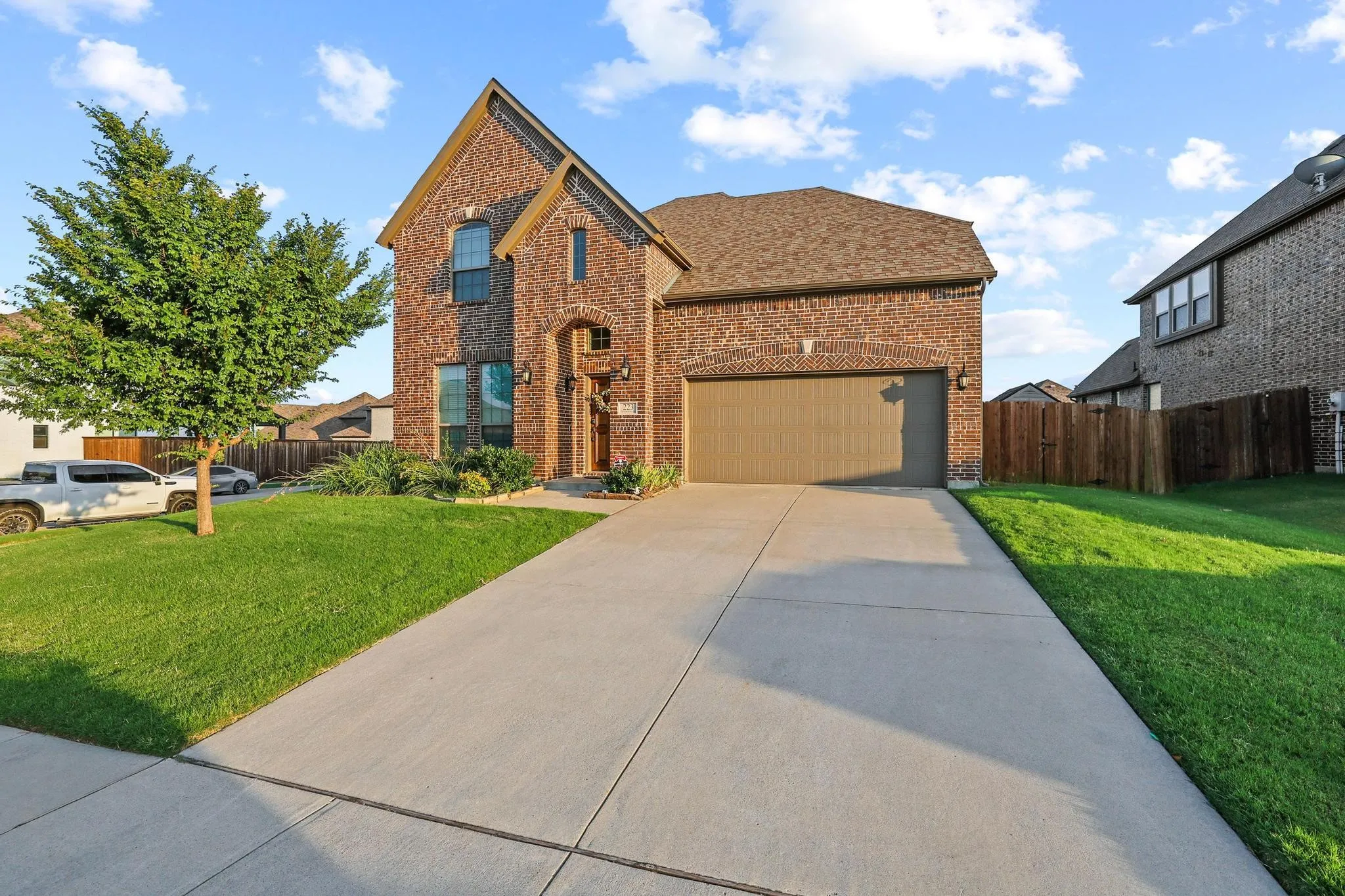 Brick exterior with an arched entry, a concrete driveway, an attached garage, a manicured lawn, and landscaping