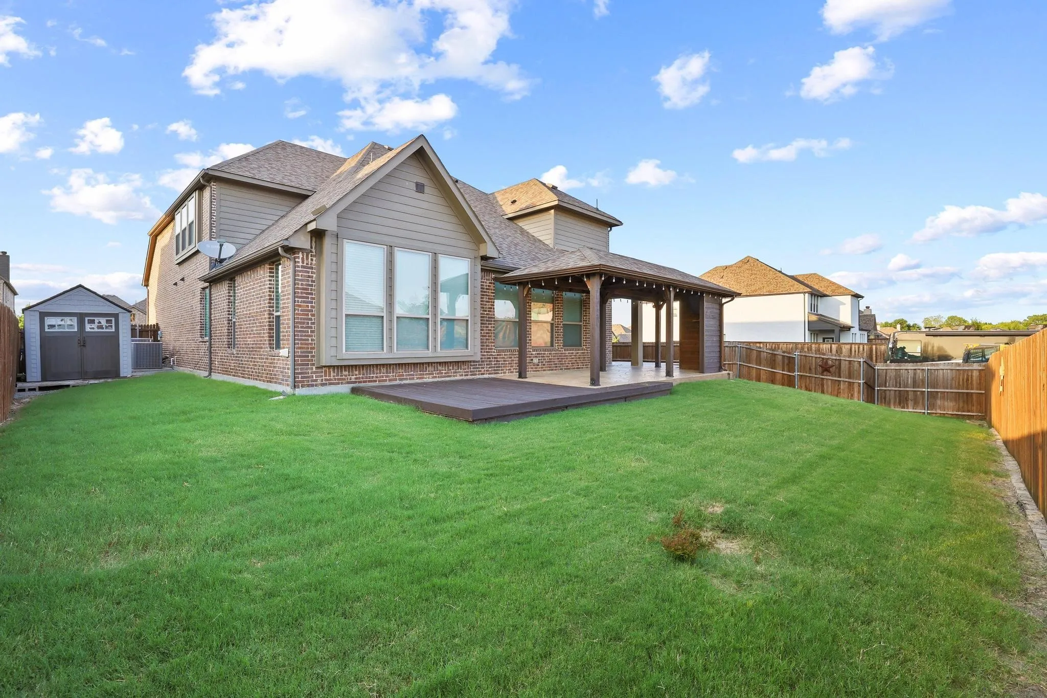 Expansive backyard featuring a covered patio, an additional open deck area, and a detached storage shed