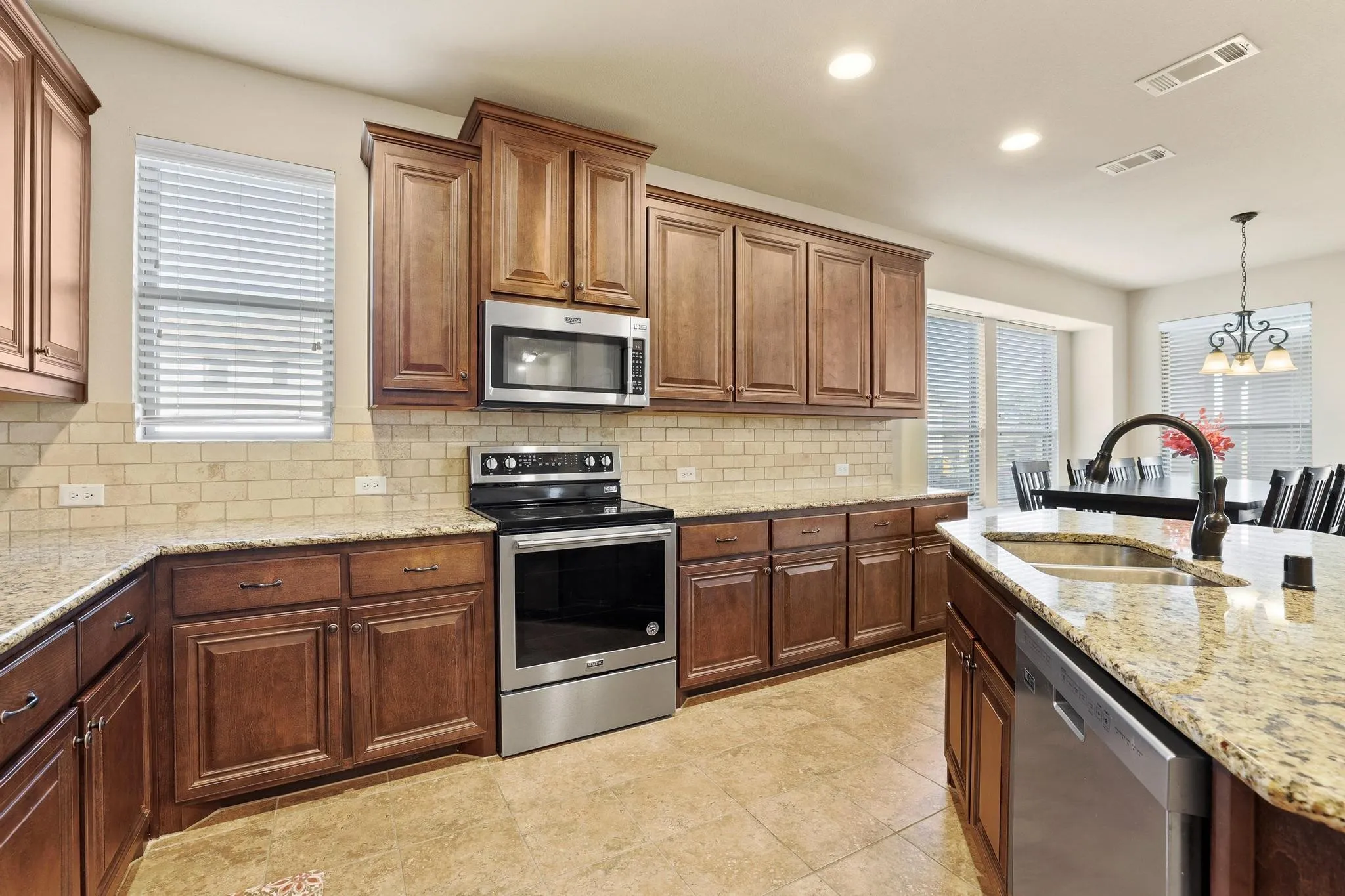 Kitchen featuring an island with a double basin sink and gooseneck faucet, stainless steel appliances, wood cabinetry, granite countertops, and tile backsplash
