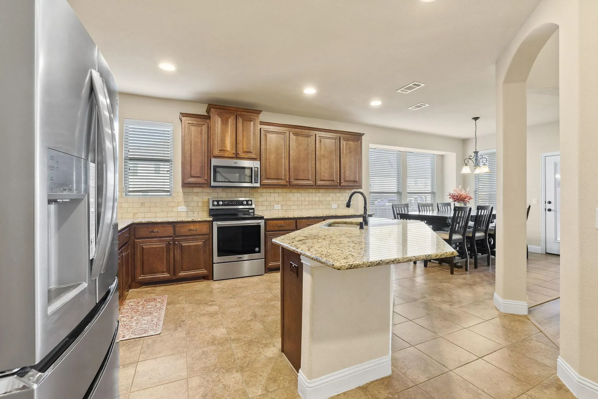 Kitchen featuring a central island with granite countertop, wood cabinetry, stainless steel appliances, and a tiled backsplash