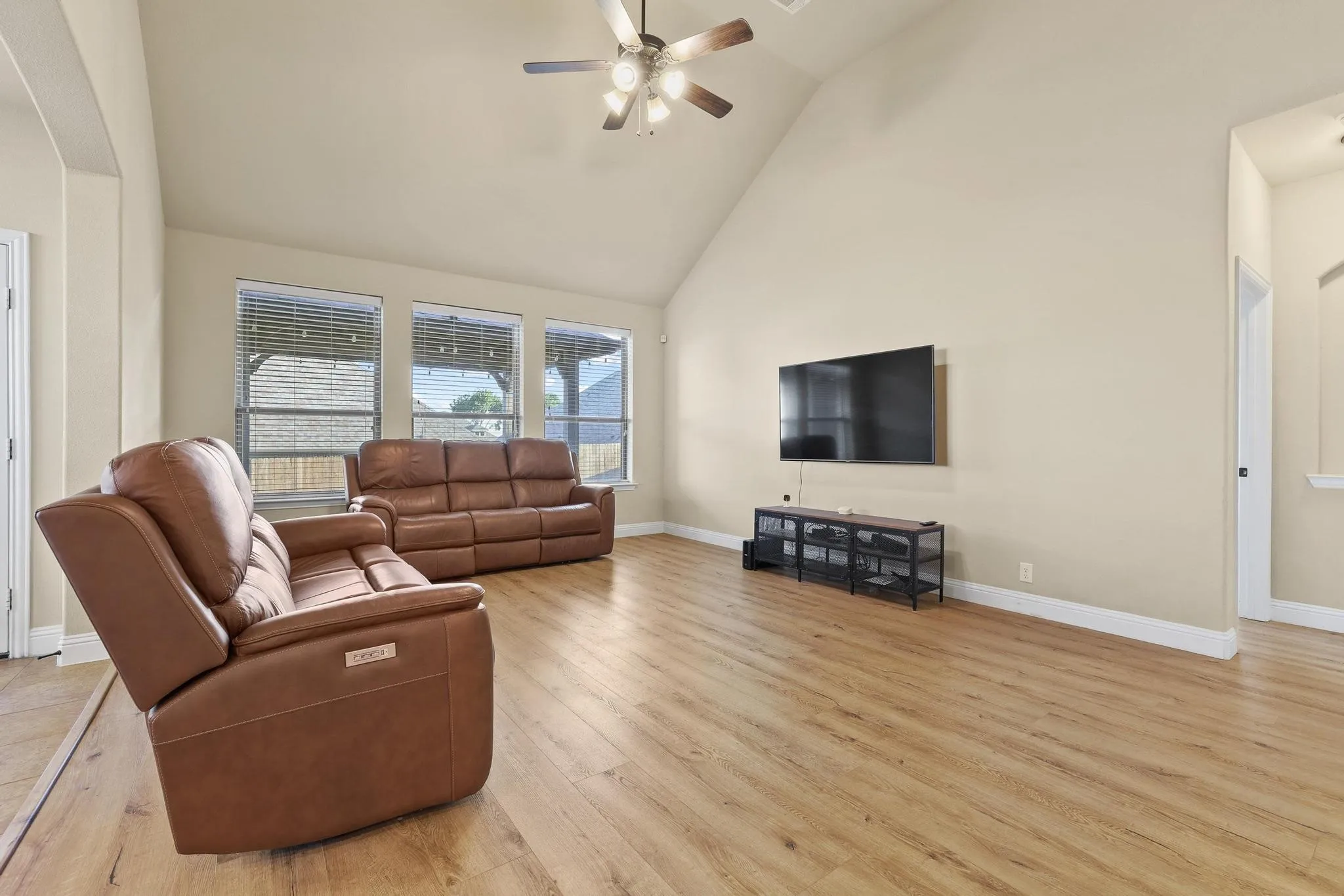 Expansive living area featuring vaulted ceilings, wood-finish flooring, and multiple windows with blinds