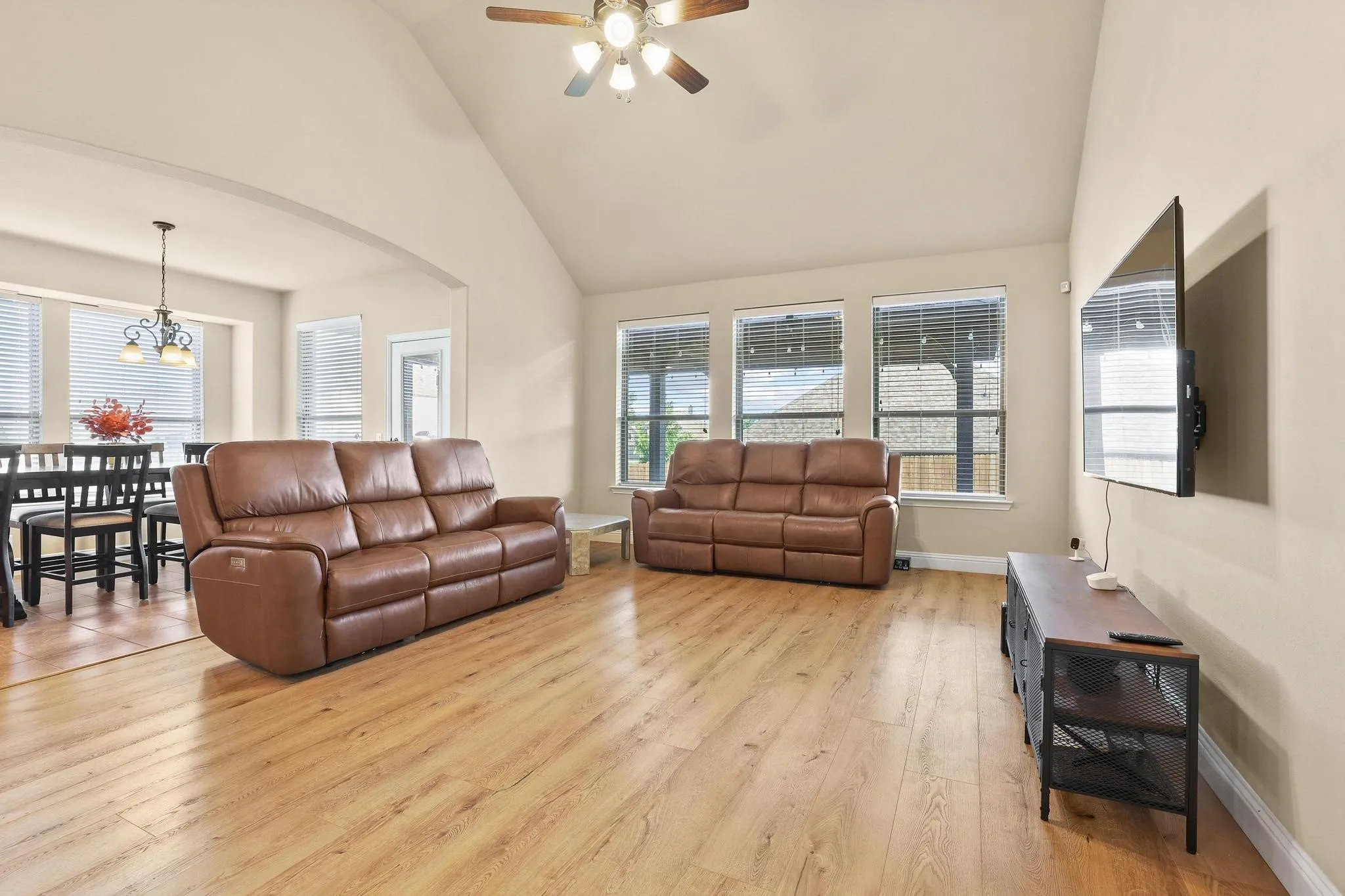 Open-concept living area featuring wood-finish flooring, vaulted ceilings, and a ceiling fan with integrated lighting