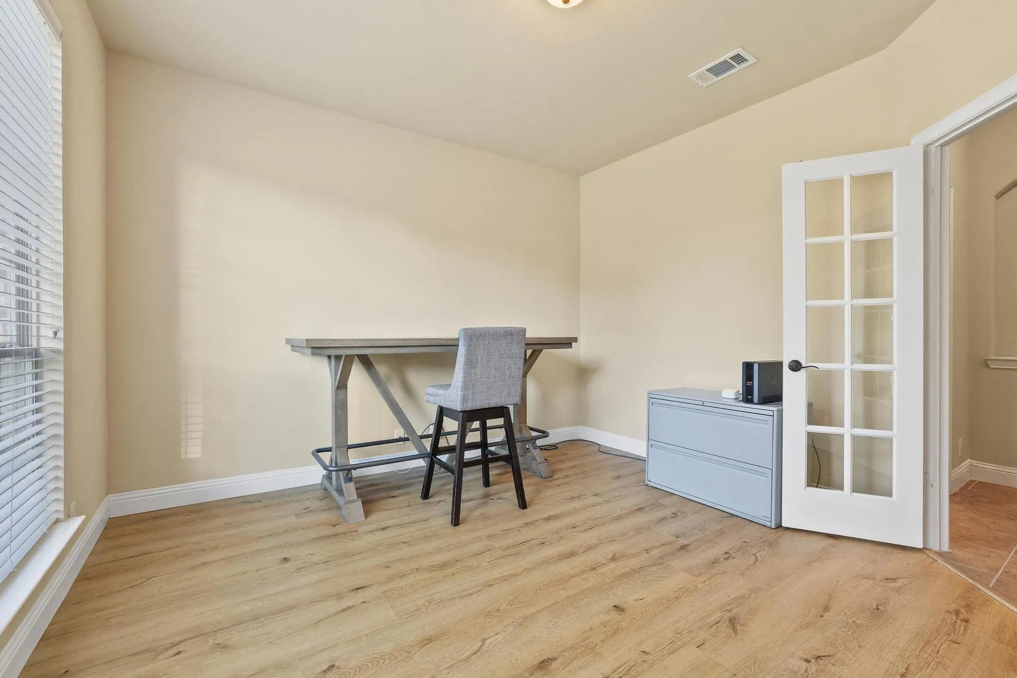 Room with wood-finish flooring, neutral wall paint, white baseboards, and a white French door with clear glass panels