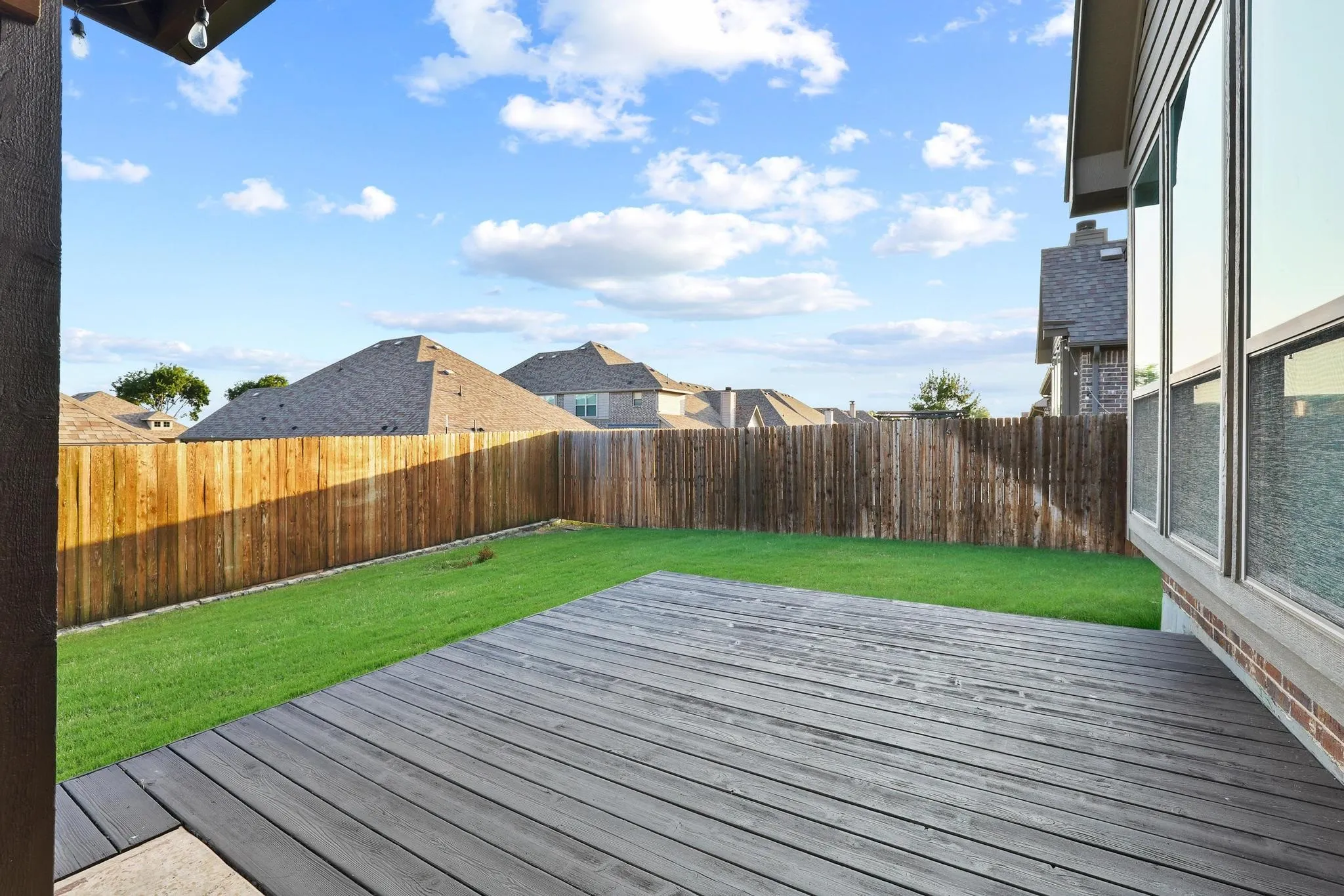 Expansive composite deck featuring a privacy fence, green lawn, and multi-pane windows