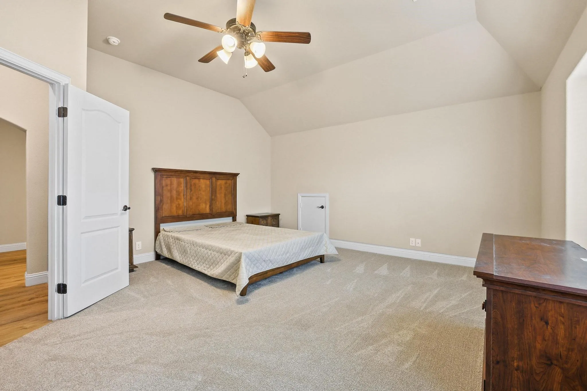 Spacious room featuring vaulted ceilings, light-colored carpeting, and a ceiling fan with integrated lighting