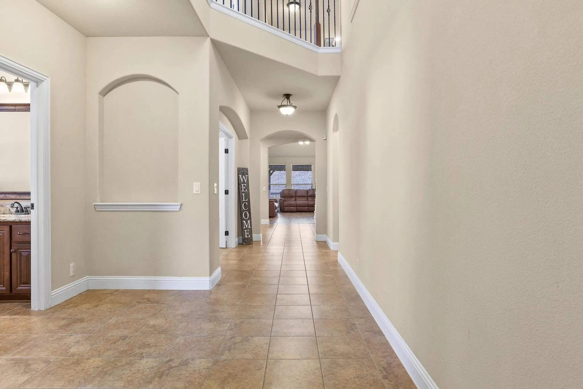 Entry foyer featuring tile flooring, neutral wall tones, arched wall niche, and an open staircase with dark metal balusters