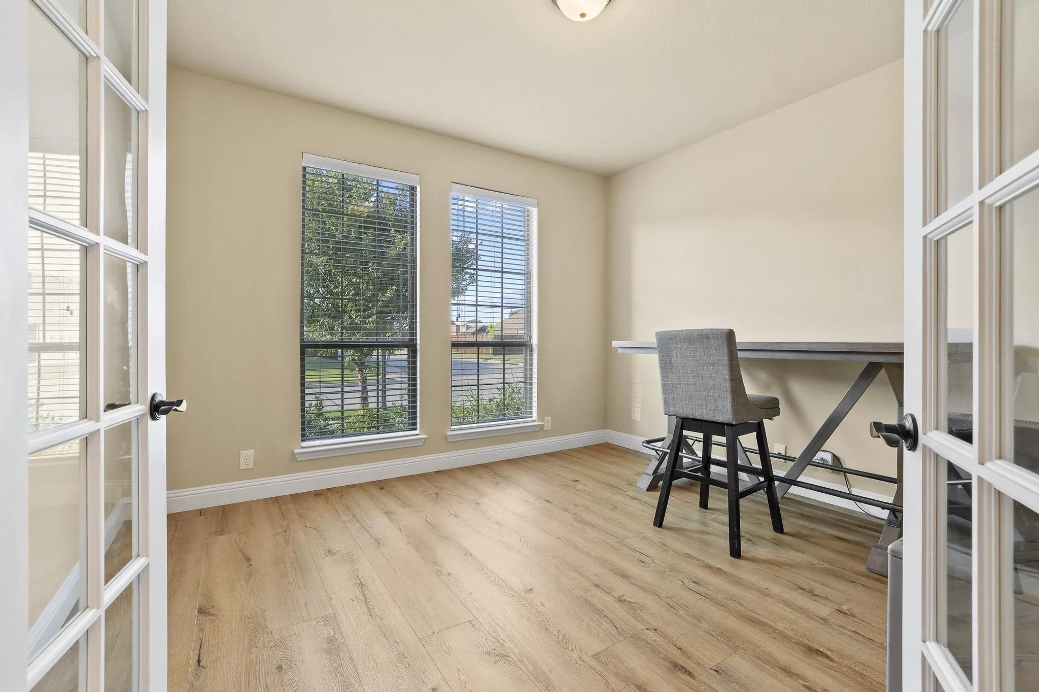Room featuring French doors, wood-finish flooring, two large windows with horizontal blinds, and a neutral wall color