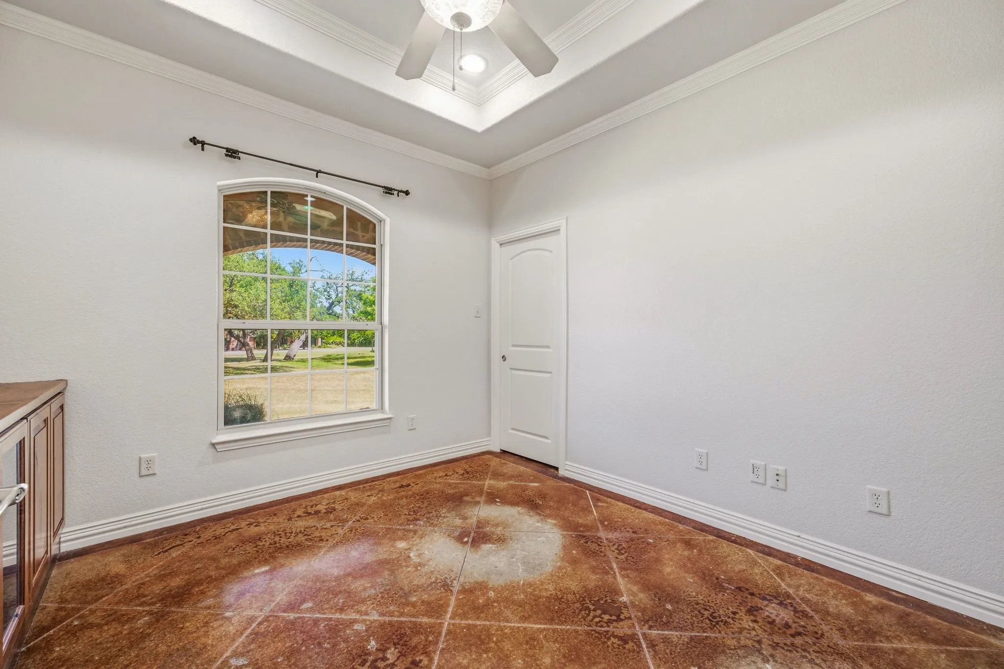 Spacious room featuring an arched window, crown molding, a tray ceiling with a ceiling fan, and tile flooring